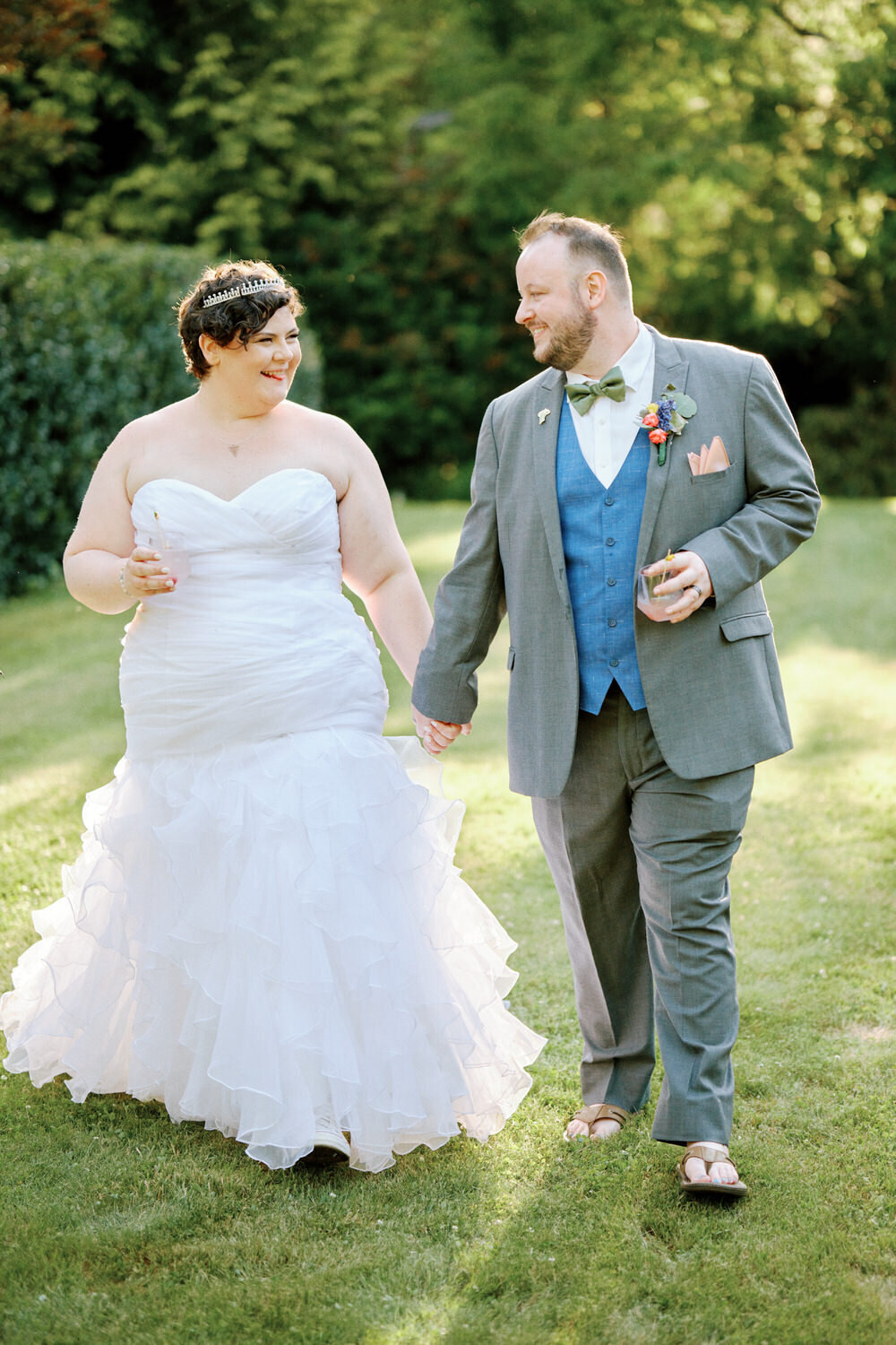 Bride and groom laugh as they hold hands and walk towards the camera
