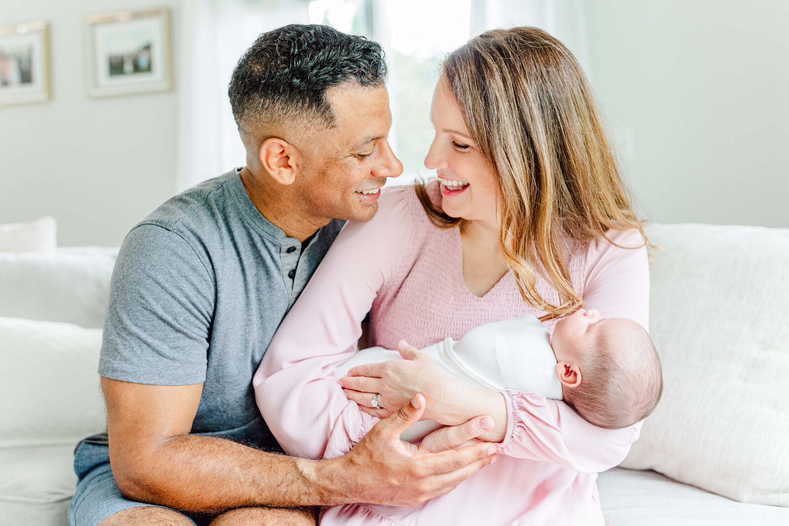 Mom and a dad sitting together on the couch and laughing while holding their newborn