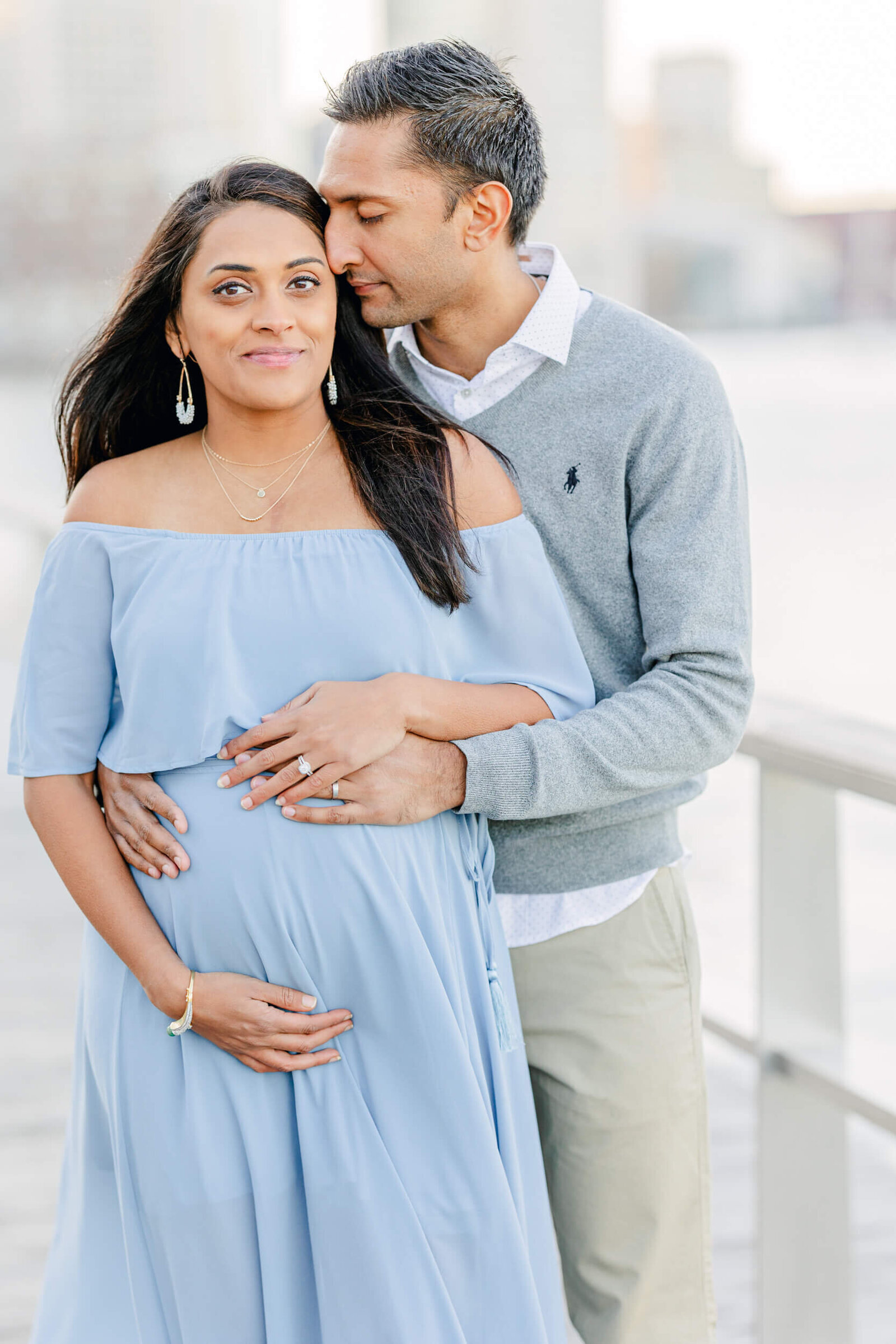 Man nuzzles his pregnant wife's temple with his nose as they both hold her baby bump