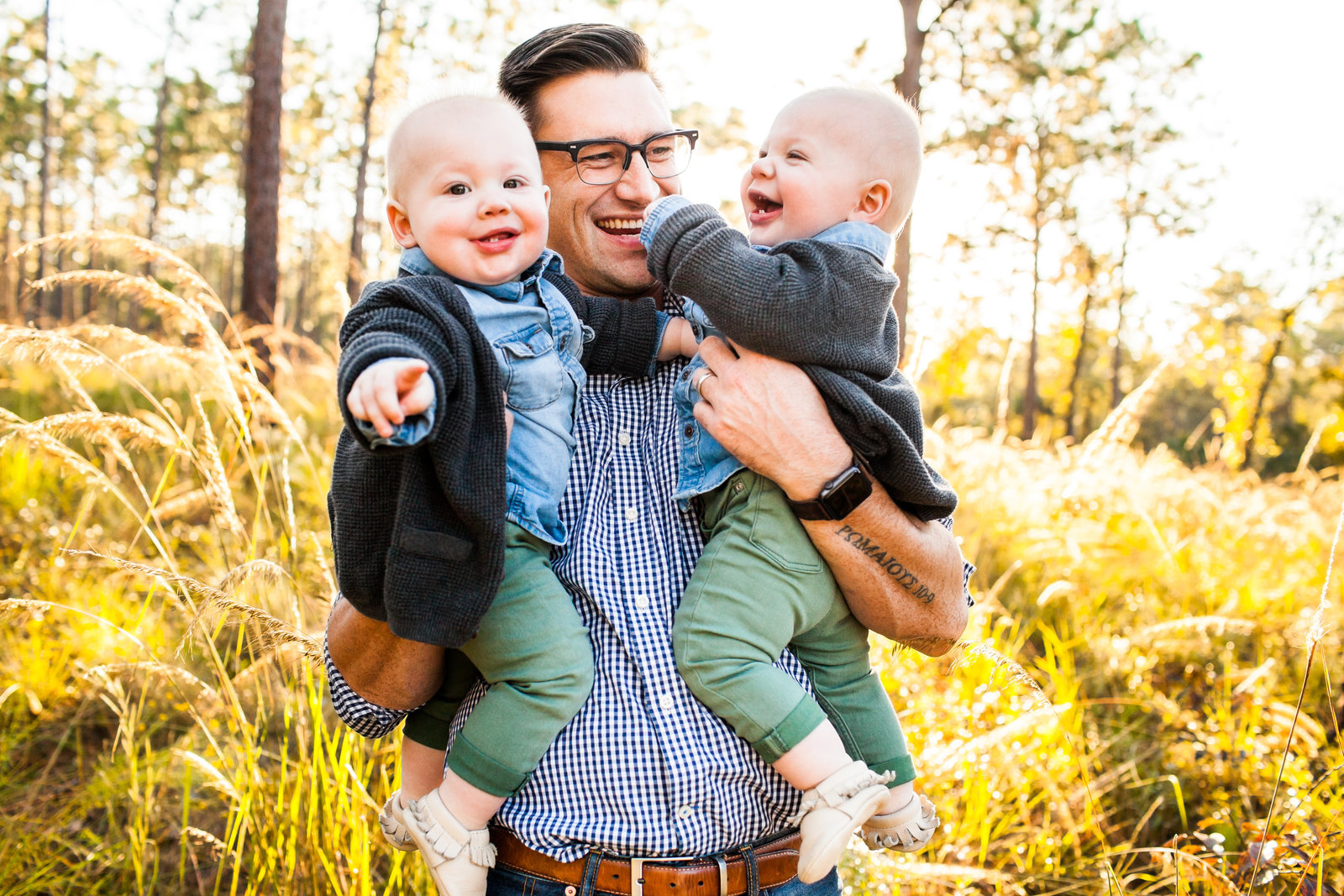 Dad holding his twin boys in field laughing