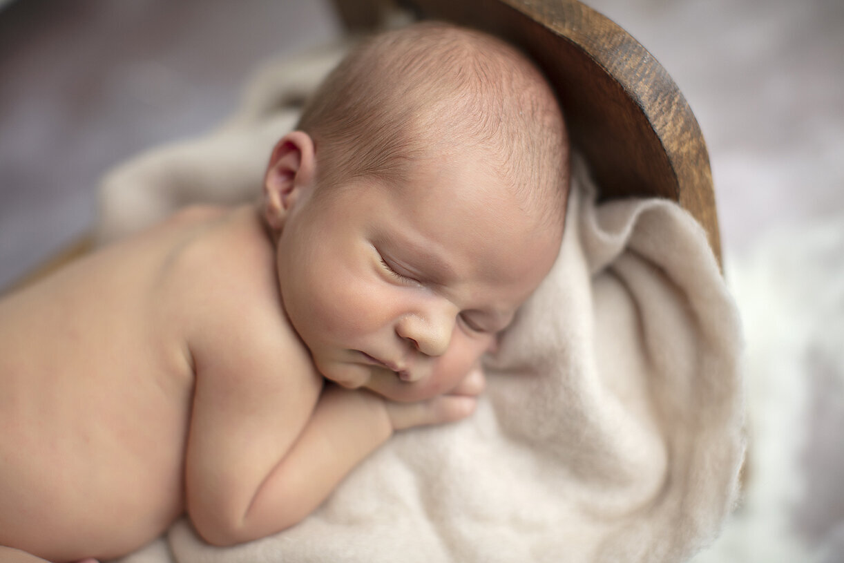 Newborn posed in small wooden bed.