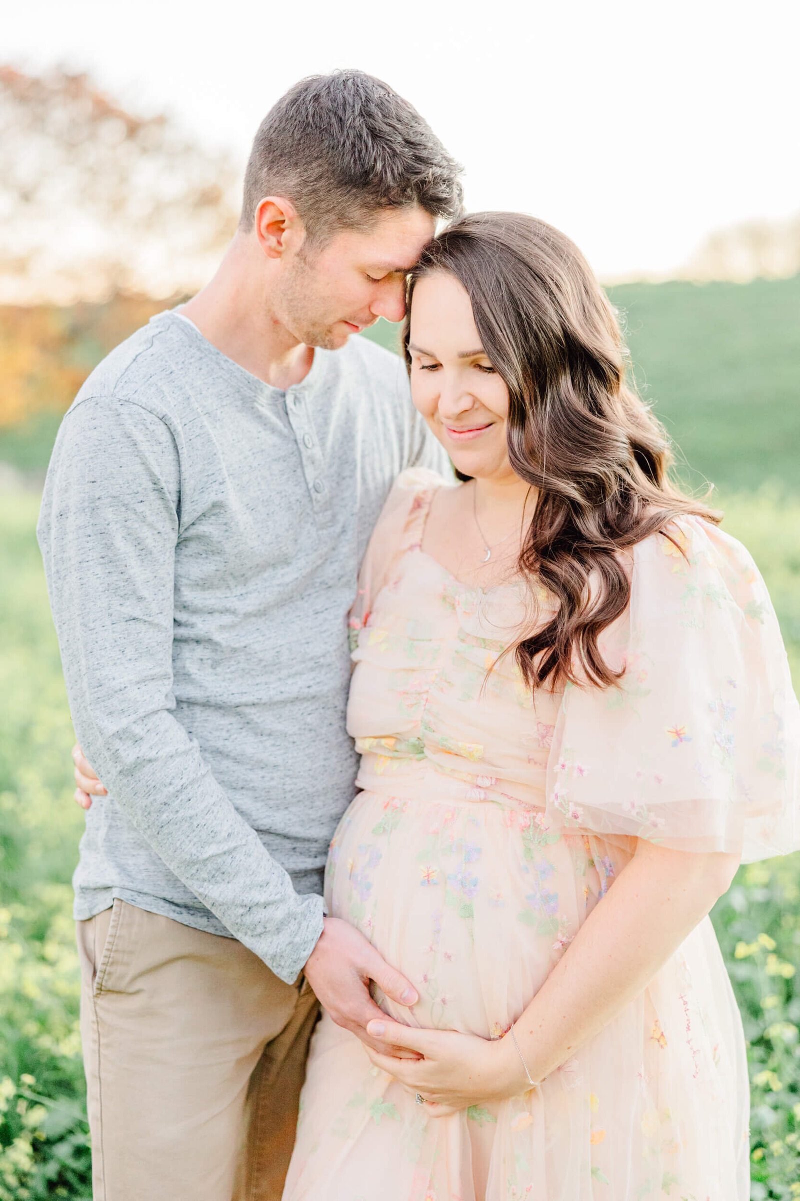 Pregnany woman and her husband nuzzle their foreheads in a field of yellow flowers