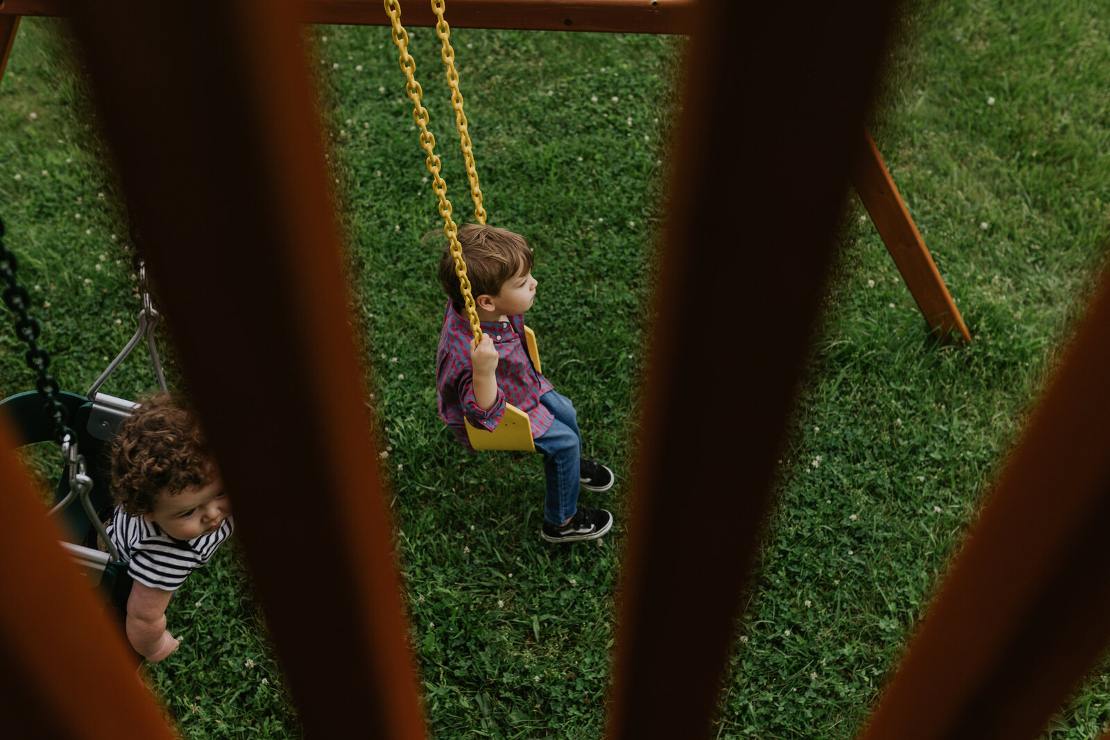 A baby and a young boy play on a swing set