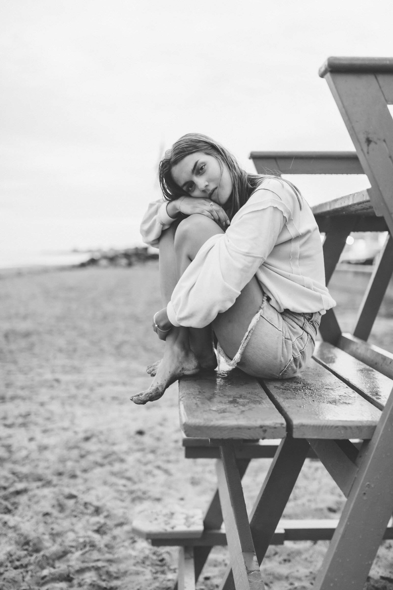 black and white photo of young woman sitting on a bench with long sleeve and jeans
