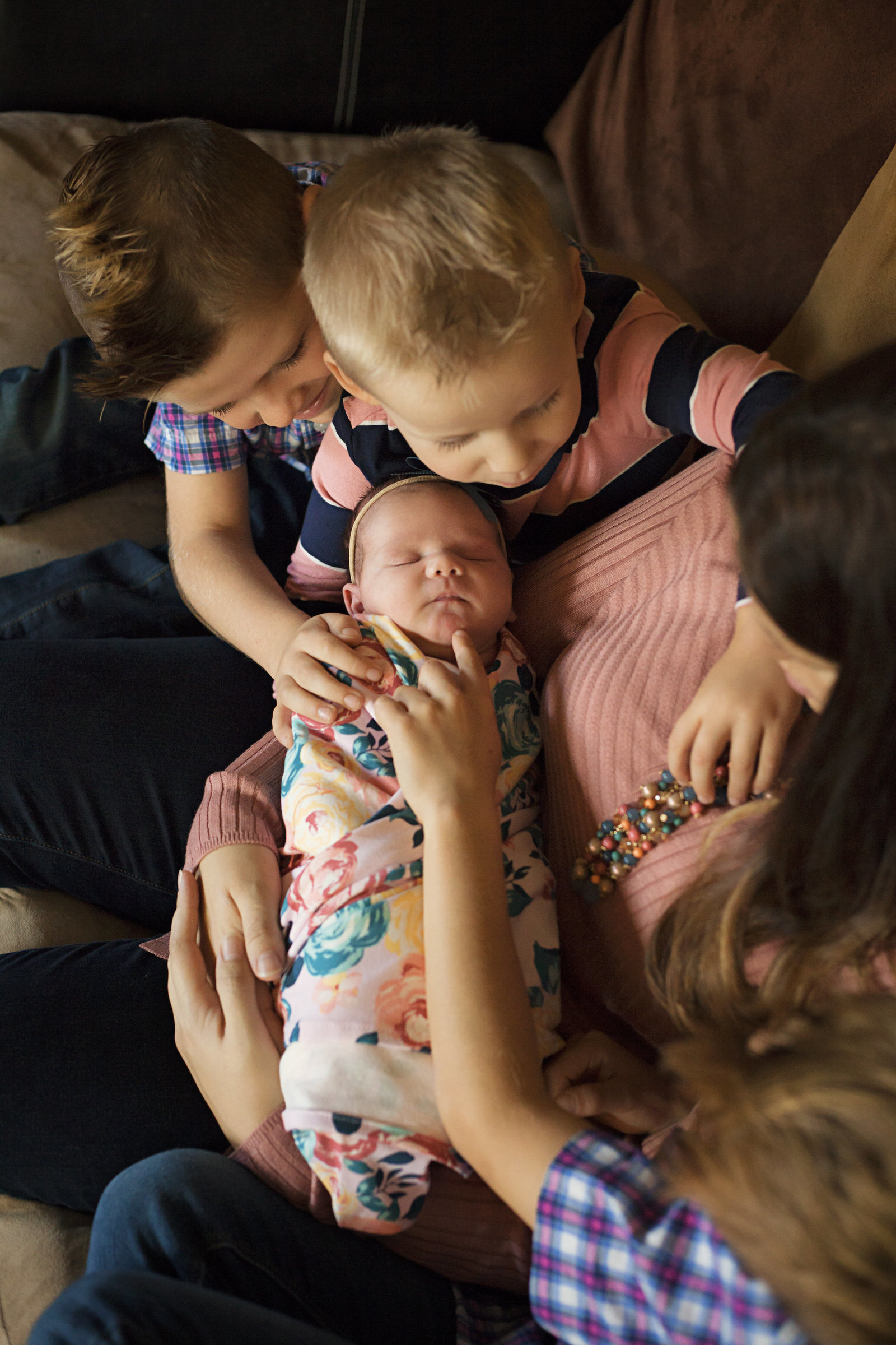 Newborn baby girl in mother's arms as three older brothers check her out.
