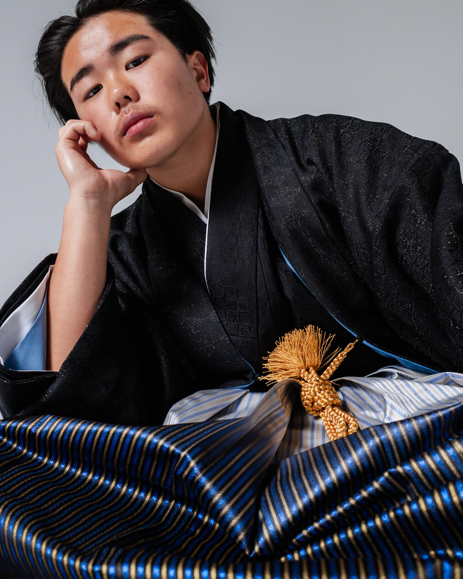 Boy in black montsuki hakama seated and resting his head on his hand for graduation portrait | 卒業式 黒紋付袴 男の子 座りポーズ ポートレート