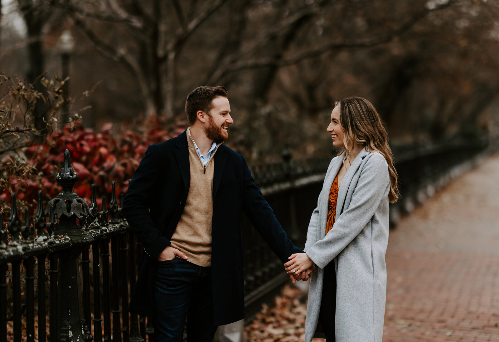 Bride and groom hold hands and look towards each other during engagement session in Boston, Massachusetts
