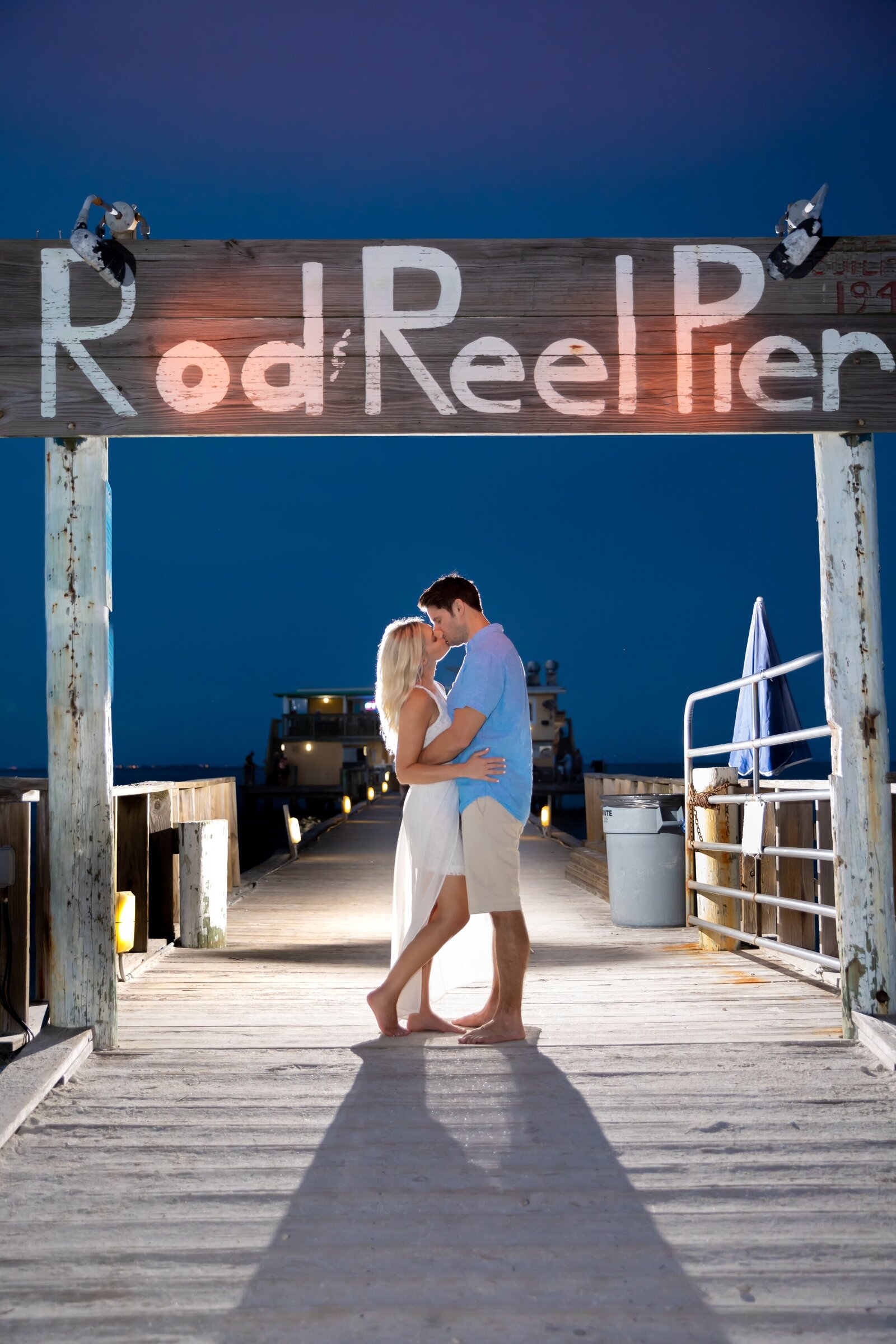 Backlit engaged couple kissing under the Rod and Reel Sign on Anna Maria Island