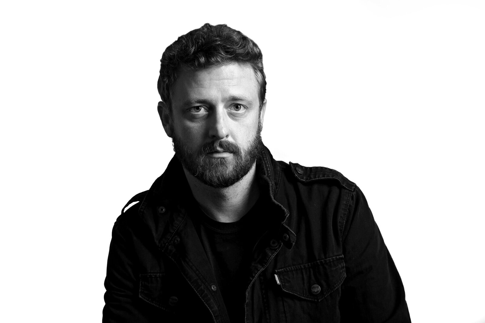Black and white portrait of a man with a beard and short curly hair, wearing a dark jacket and shirt, looking directly at the camera against a plain white background—ideal for band photography Jacksonville.