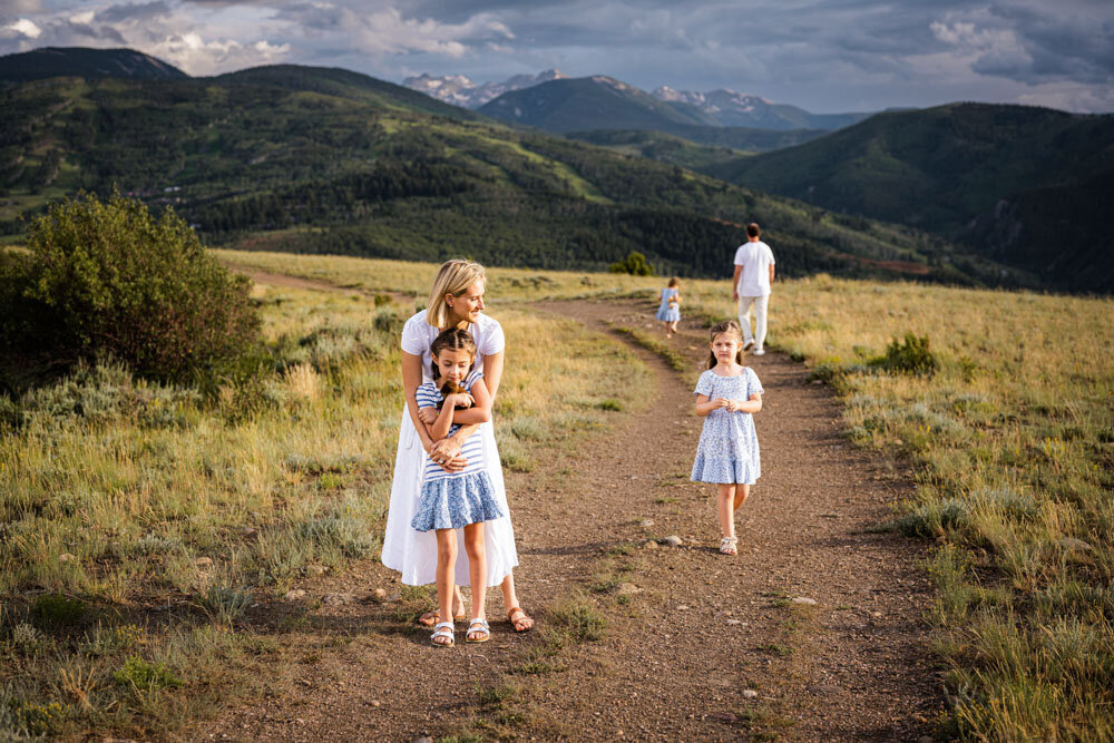 A mom and her three daughters dance in a mountain top field