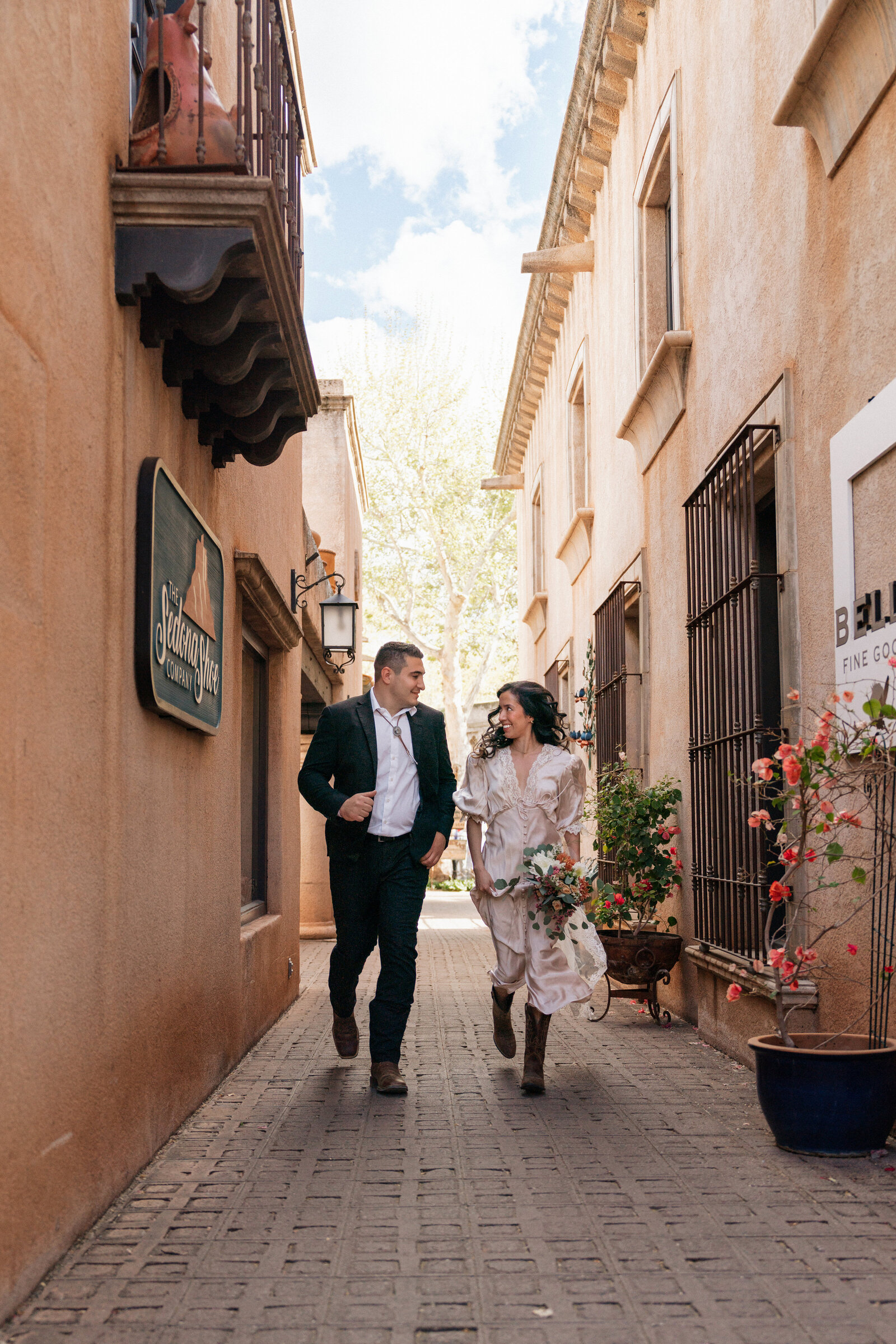 Bride and groom running hand-in-hand through the charming cobblestone alleys of Tlaquepaque Arts & Shopping Village in Sedona during their playful elopement celebration.