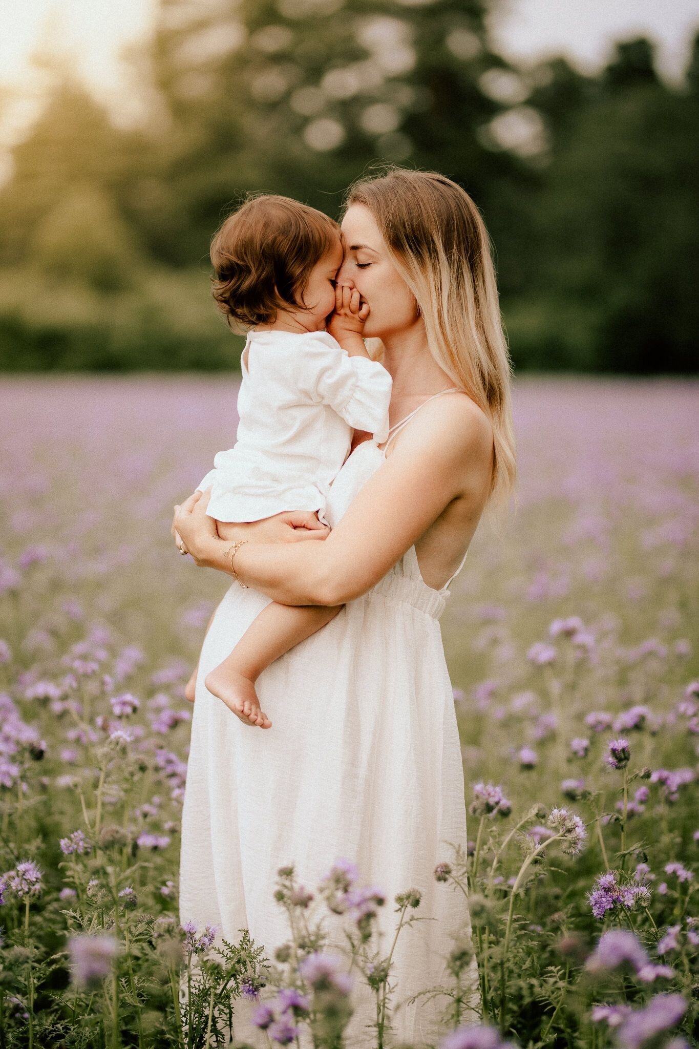 en mamma och hennes dotter pussas på ett fält med lila blommor
