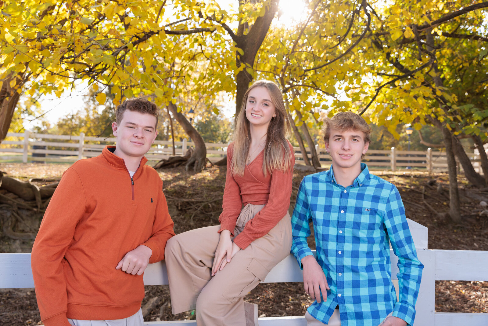 Siblings by a fence in front of a fall tree in Raleigh, NC.