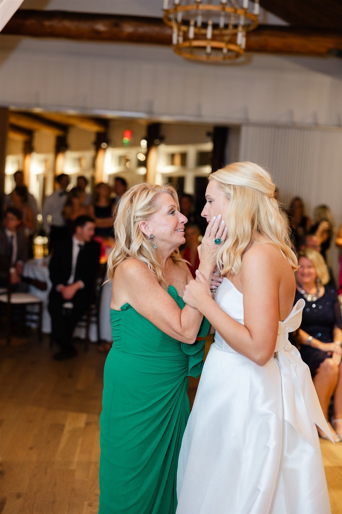 Mother holding her daughters cheek as they dance together at the daughters wedding