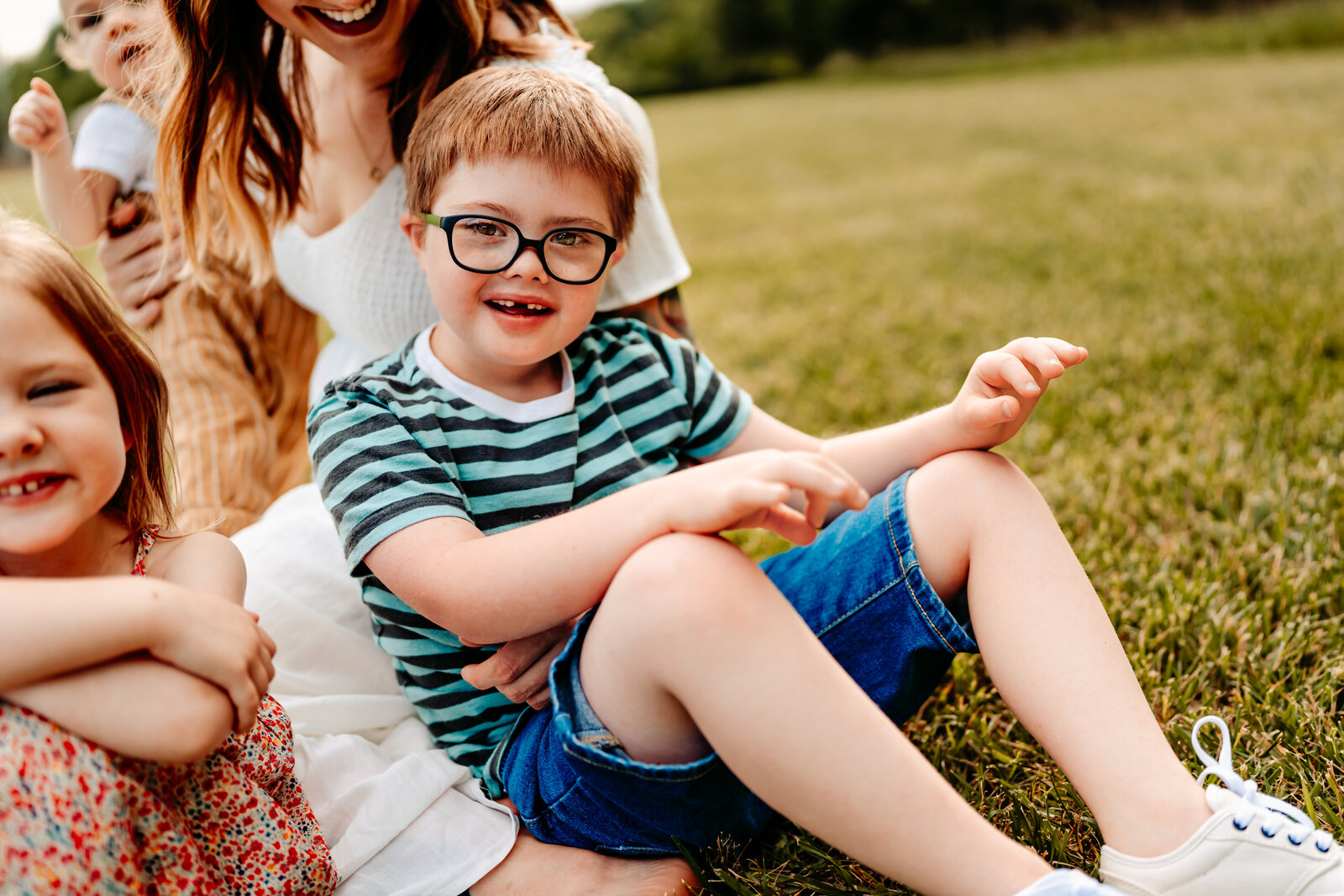 Mother sits on grassy field with daughter and sons laughing in columbus ohio