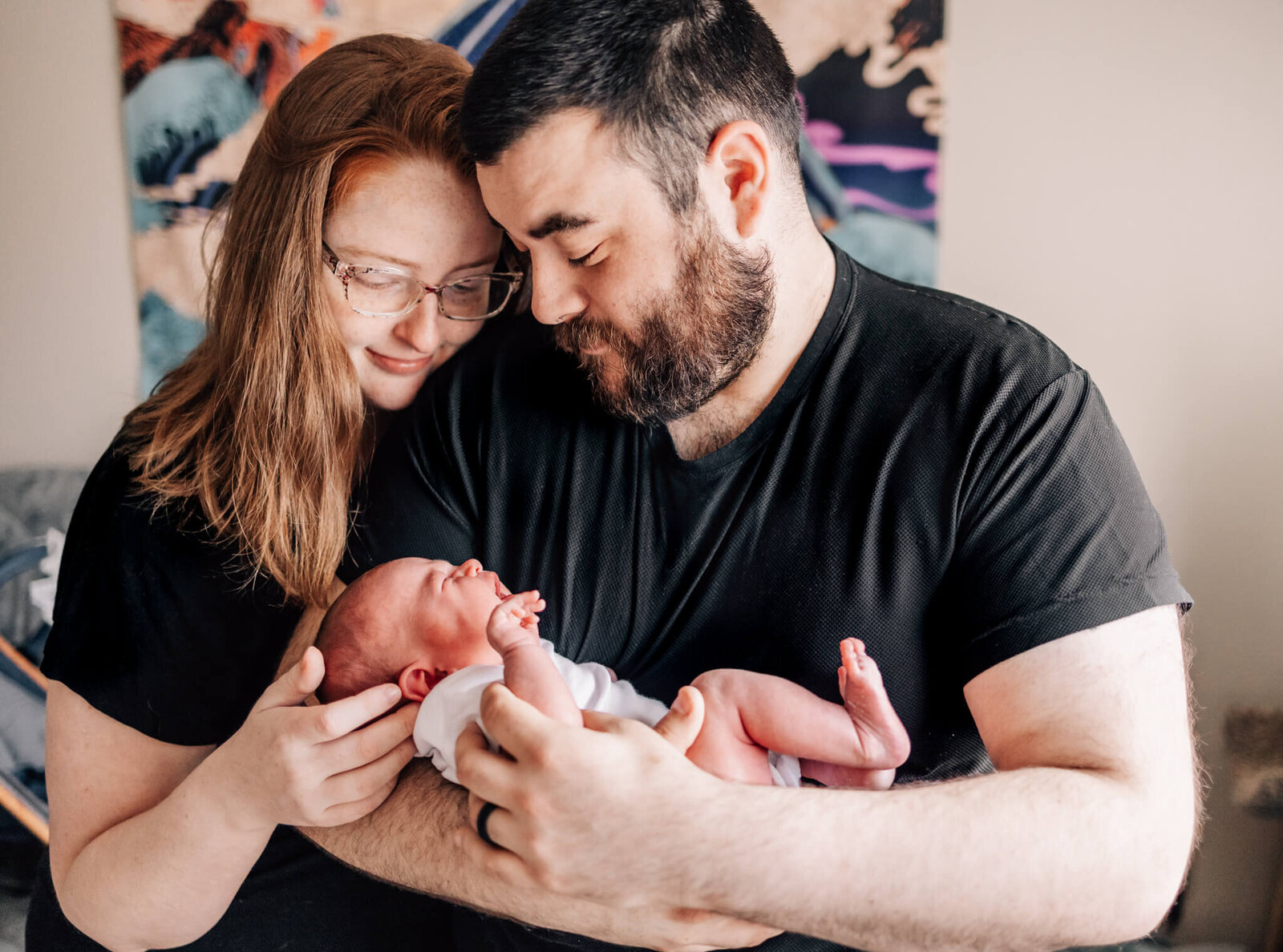 Mom and dad holding baby together, looking down at baby.