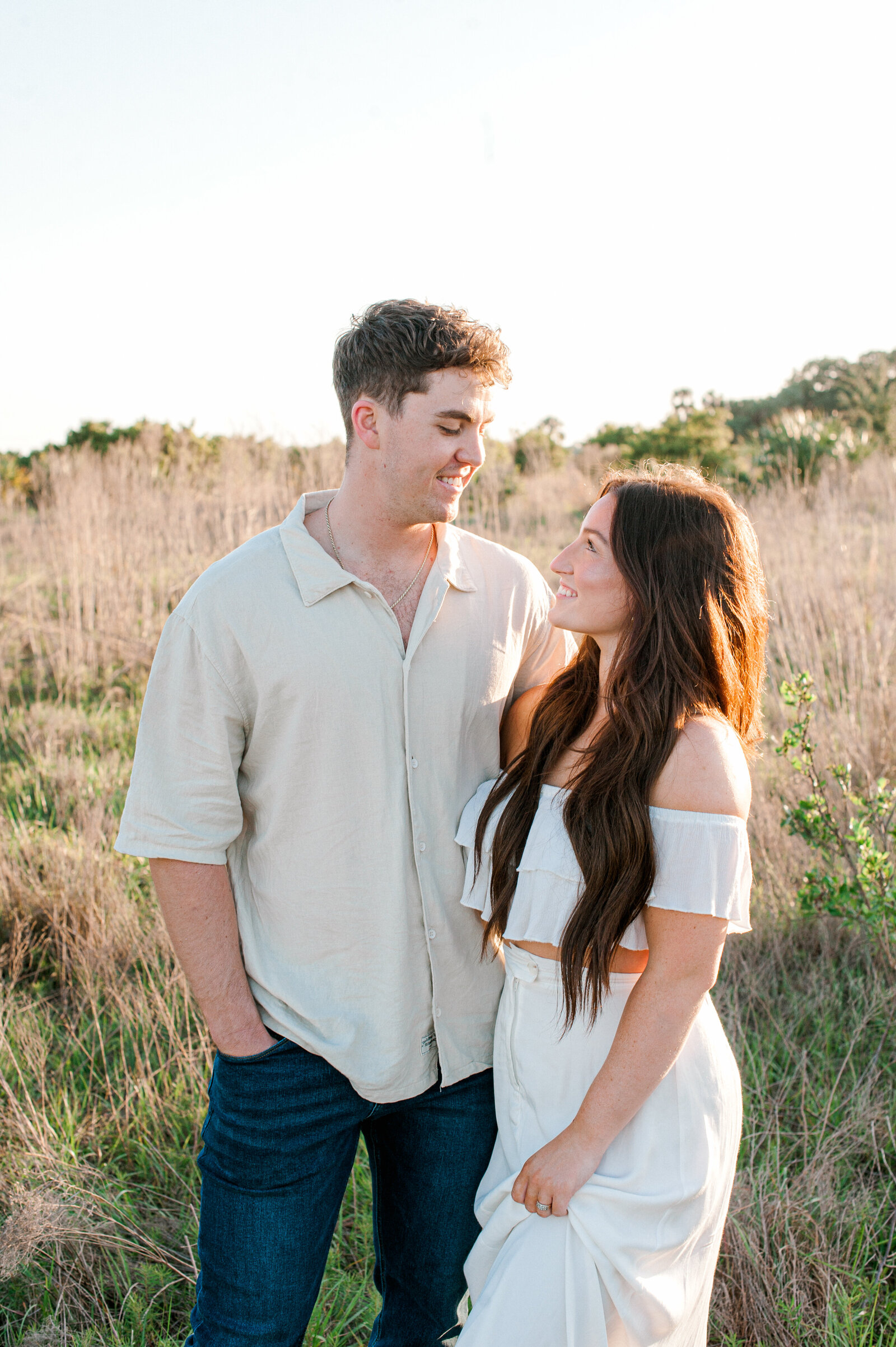 Couple smile at each other while standing in a tall grass field taken by Orlando couples photographer