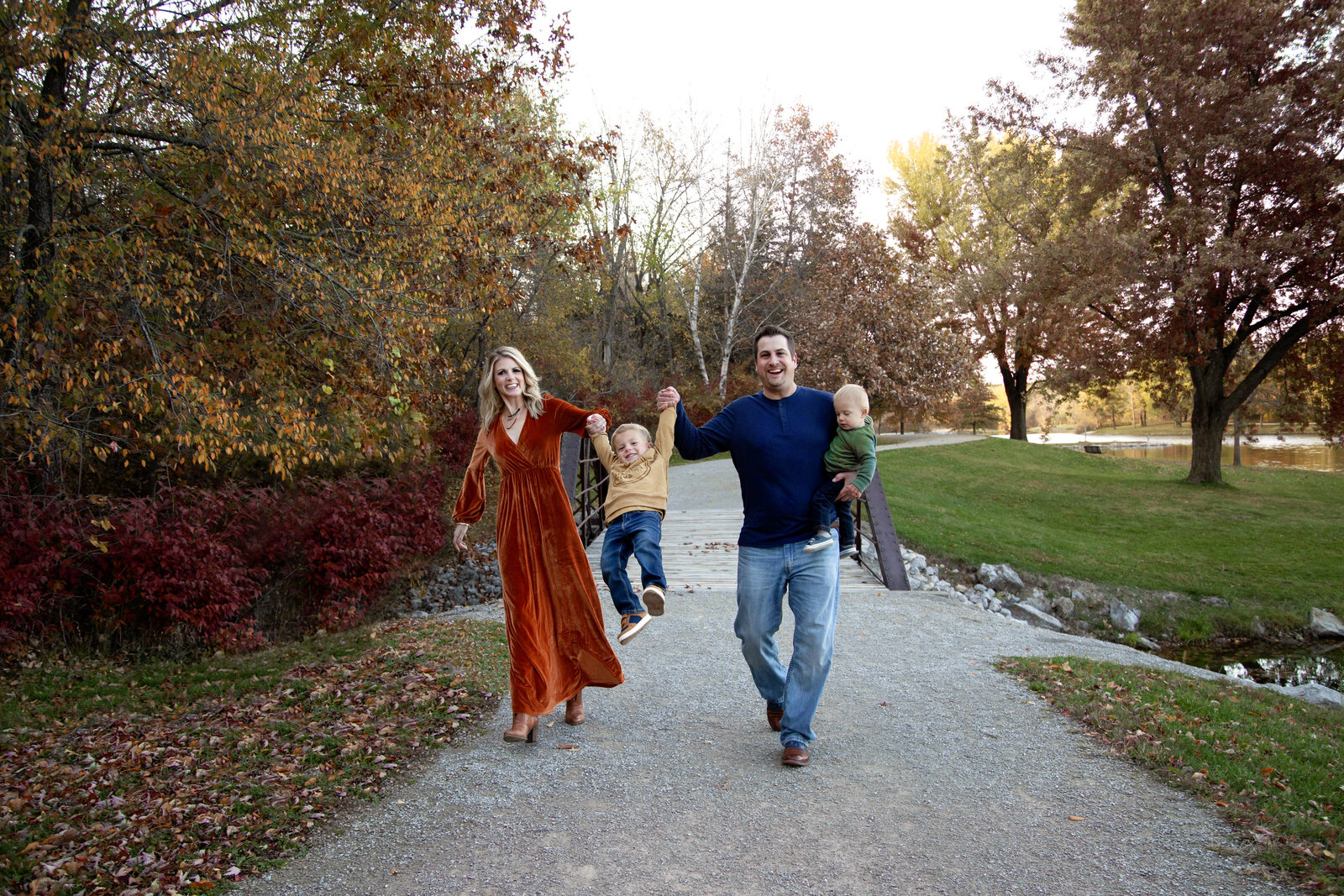 Family of four, parents swinging boy between them while walking on path.