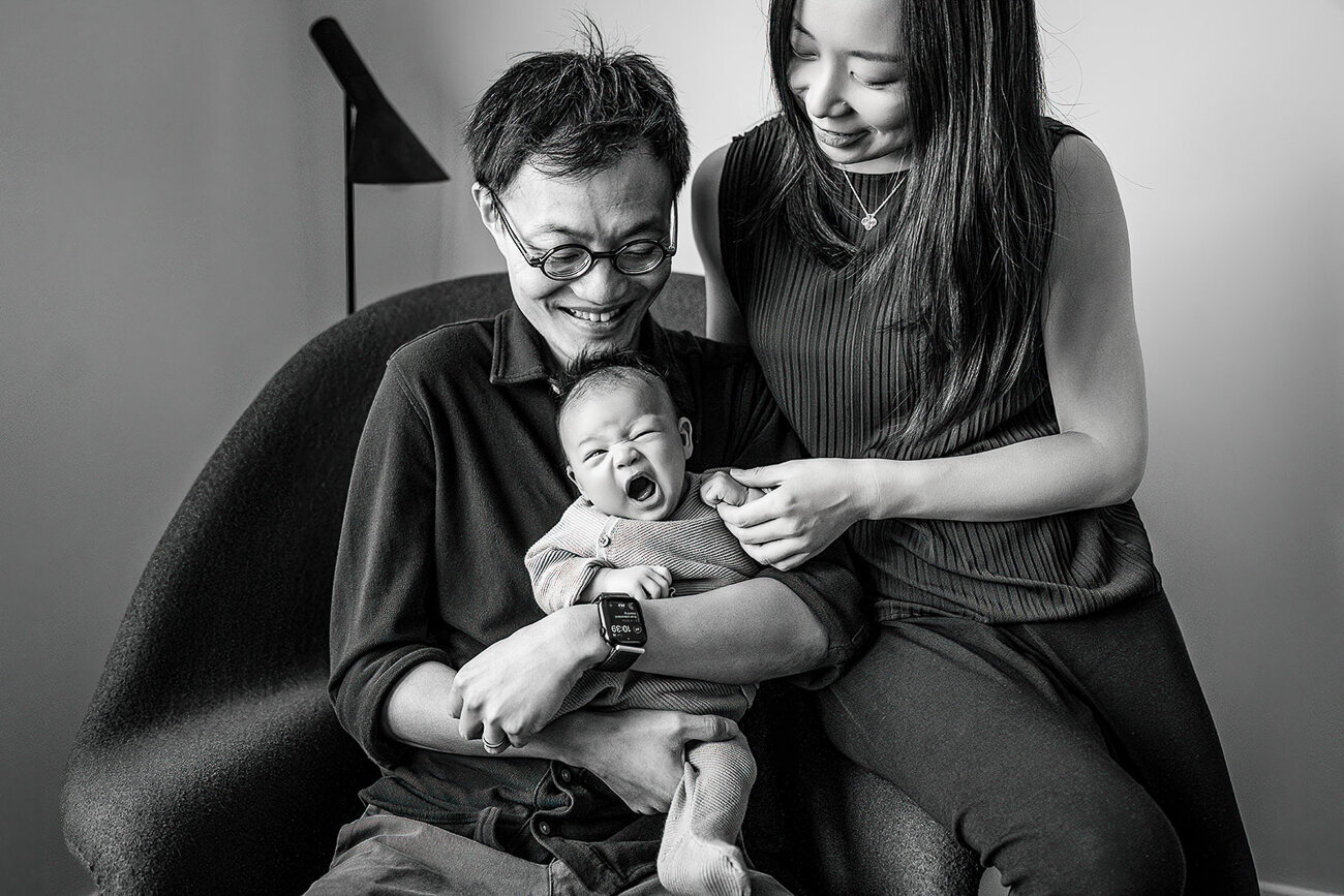 black and white portrait of new parents with yawning newborn baby