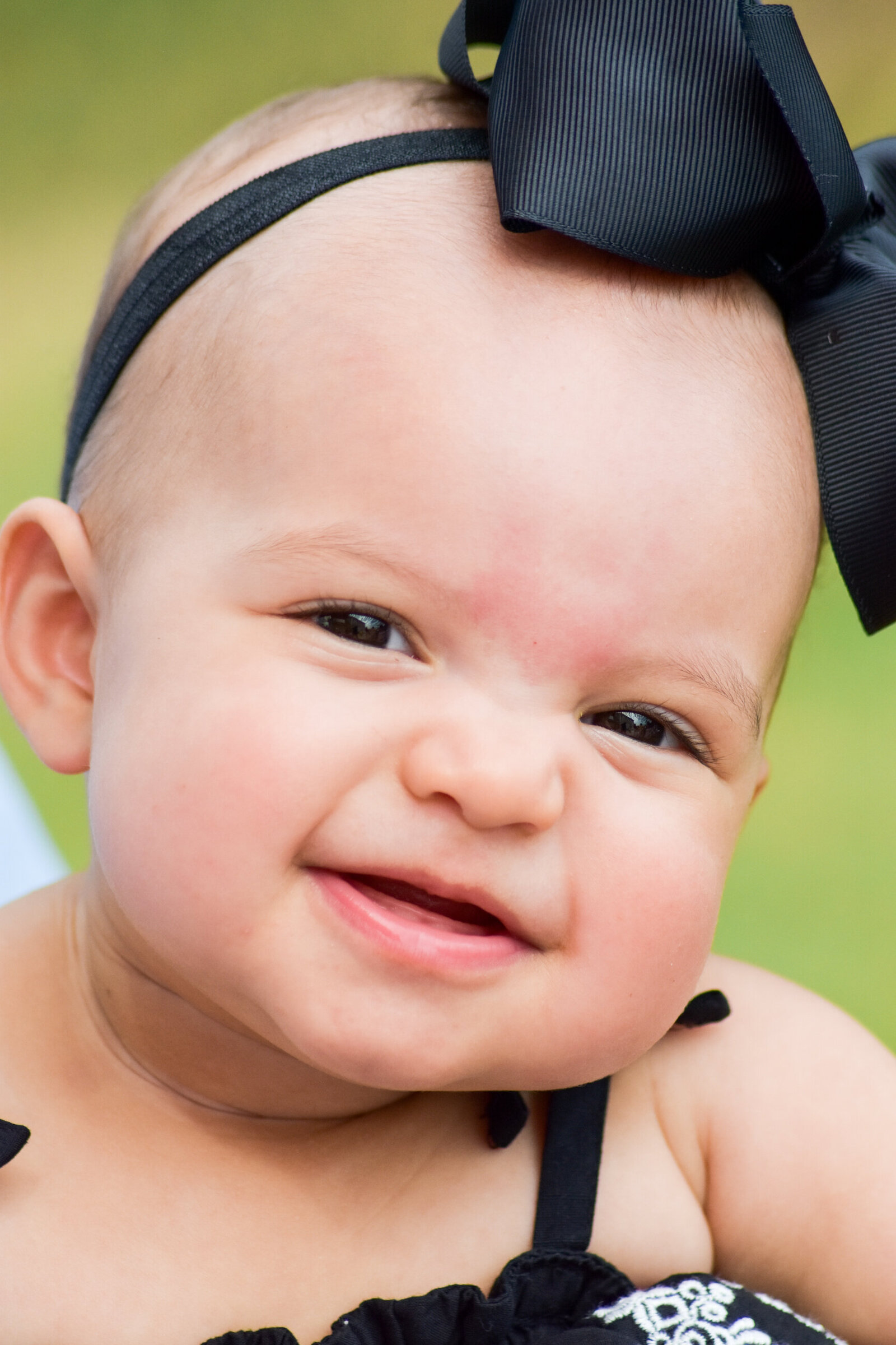 young baby girl wearing a large black bow smiling at the camera photographed by Millz Photography in Greenville, SC