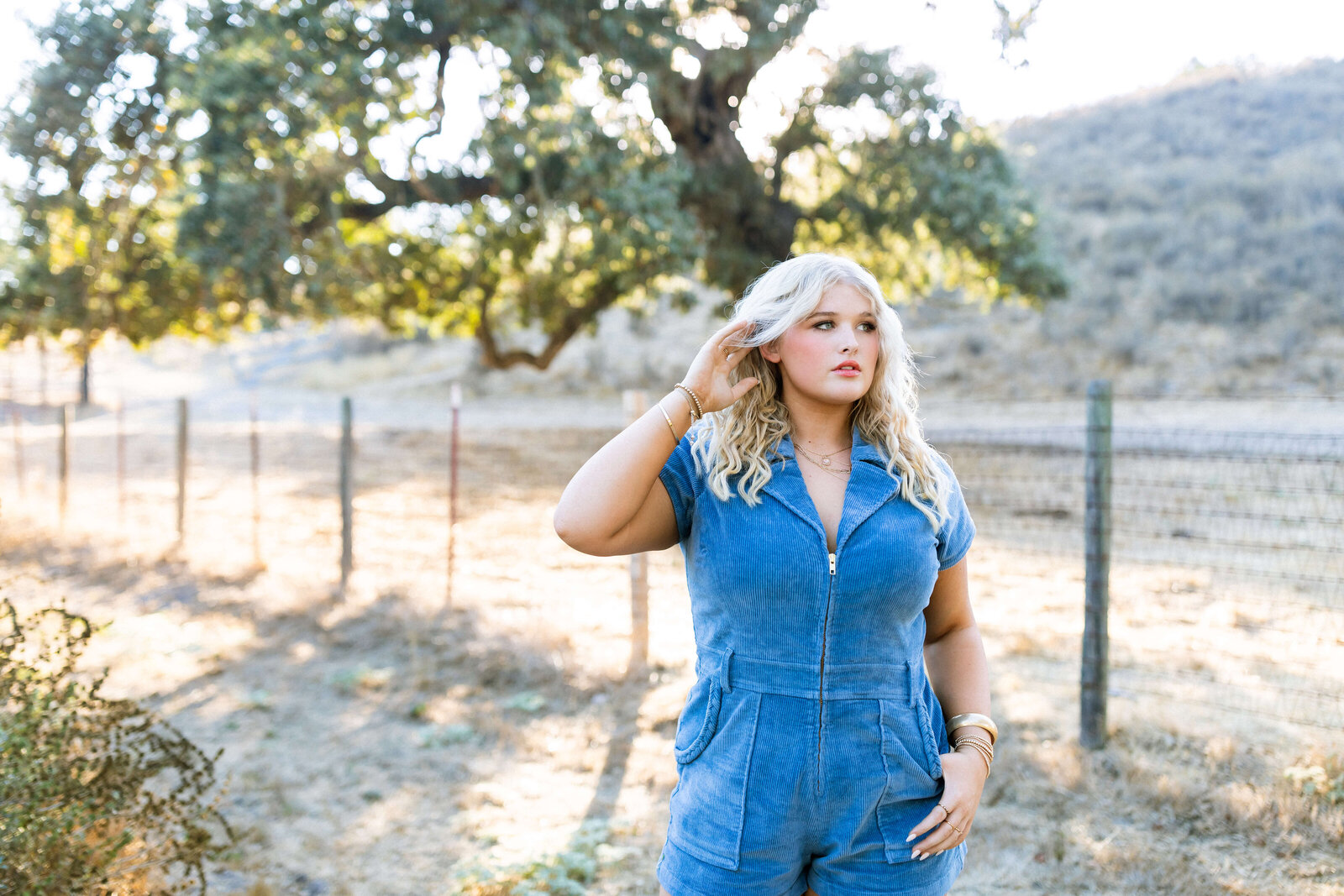 blonde girl wearing blue jean romper posing in a ranch
