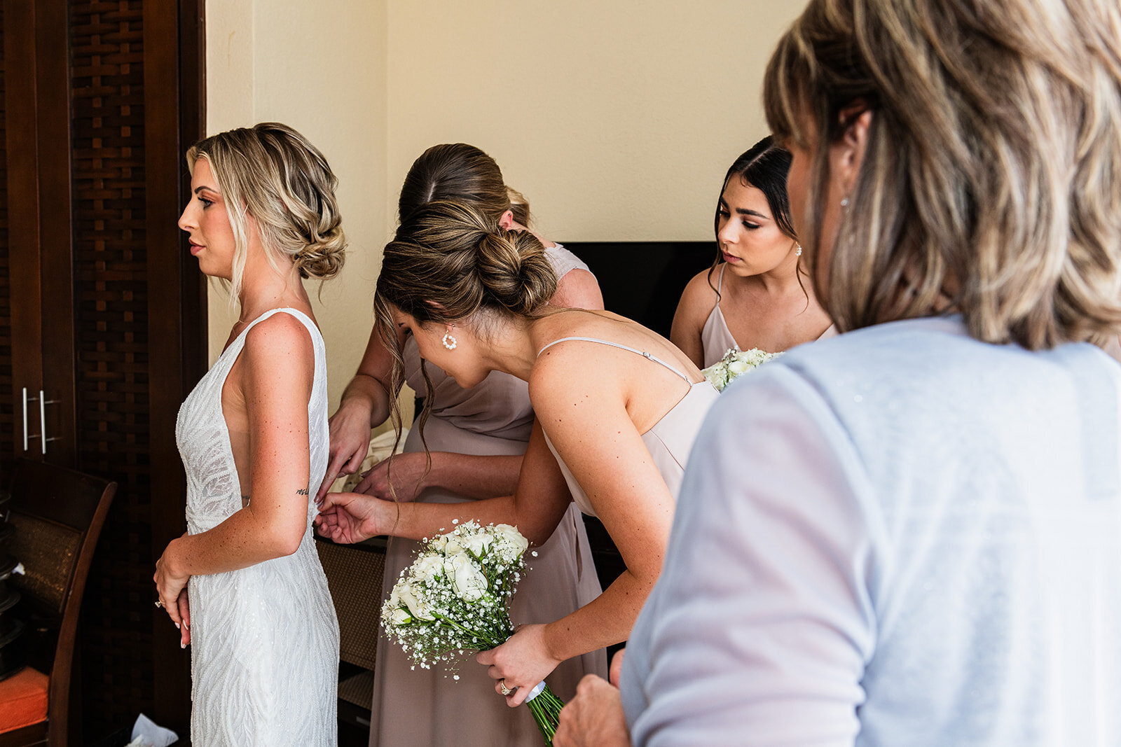 A candid moment as the bride is surrounded by her bridesmaids, helping her get ready for the wedding ceremony. Captured by CMH Studios during a destination wedding