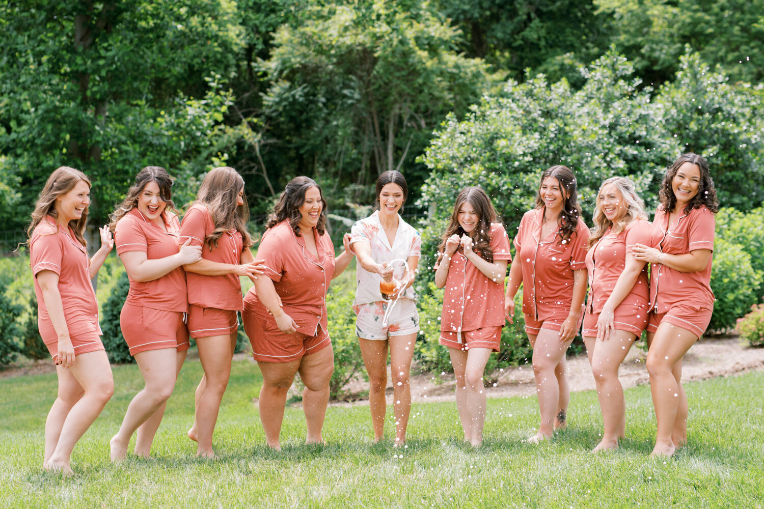 Bride and bridesmaids in matching pajamas popping champagne