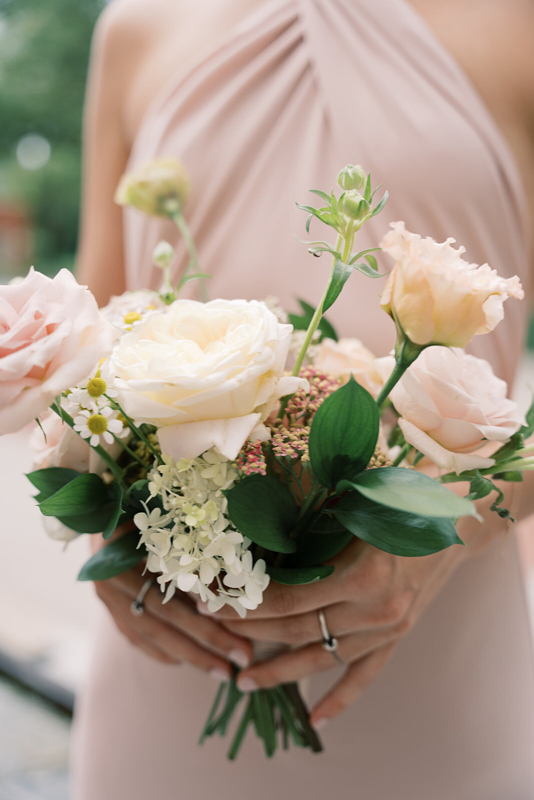 Bridesmaid holding bouquet with white hydrangea, blush lisianthus, cream garden roses, and daisies.