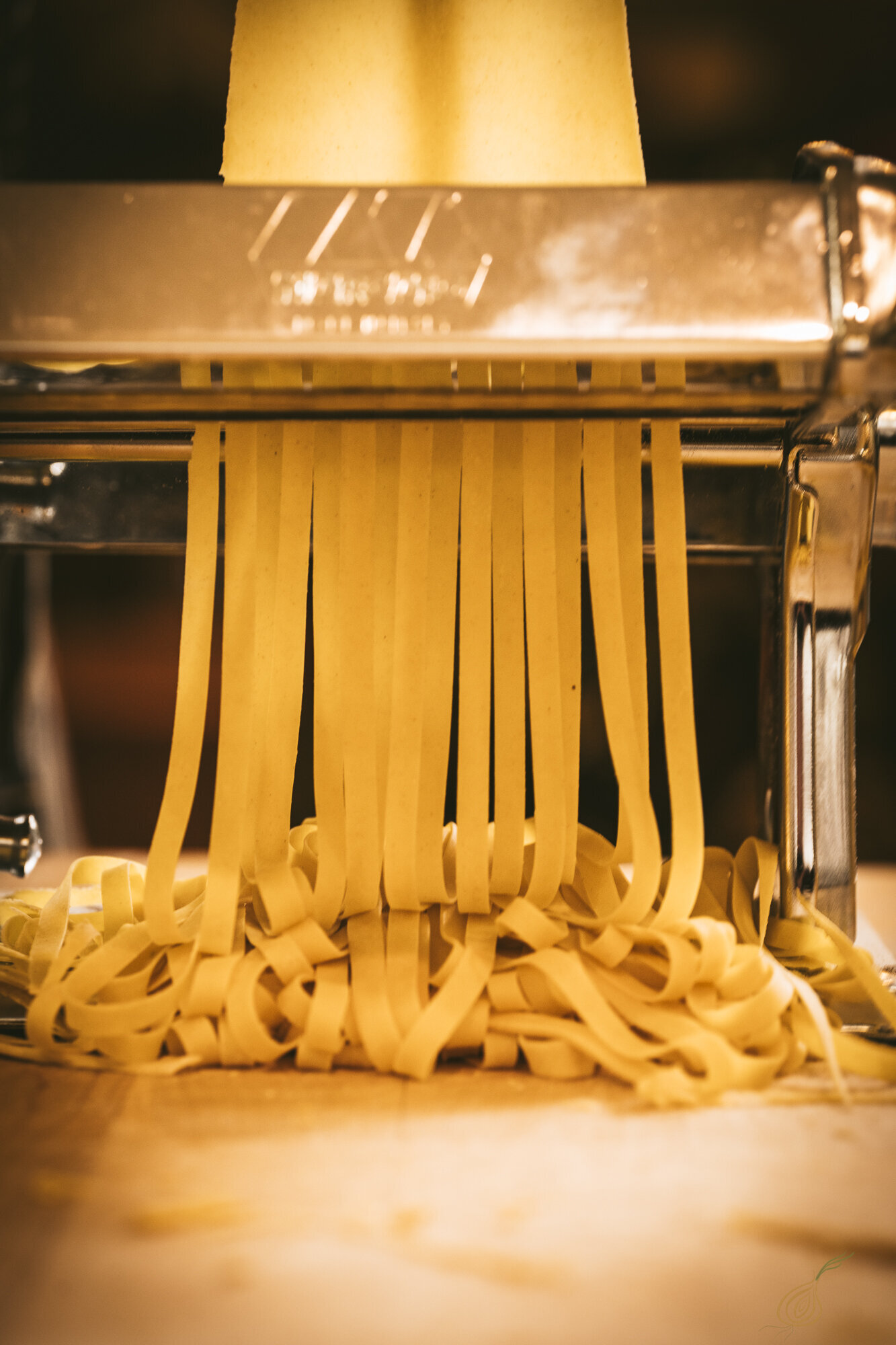 A pasta-making machine in action, producing fresh strands of pasta in a kitchen setting.