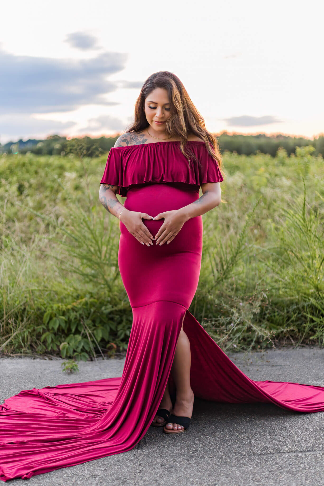 A pregnant woman standing in a field holding her hands over her belly.