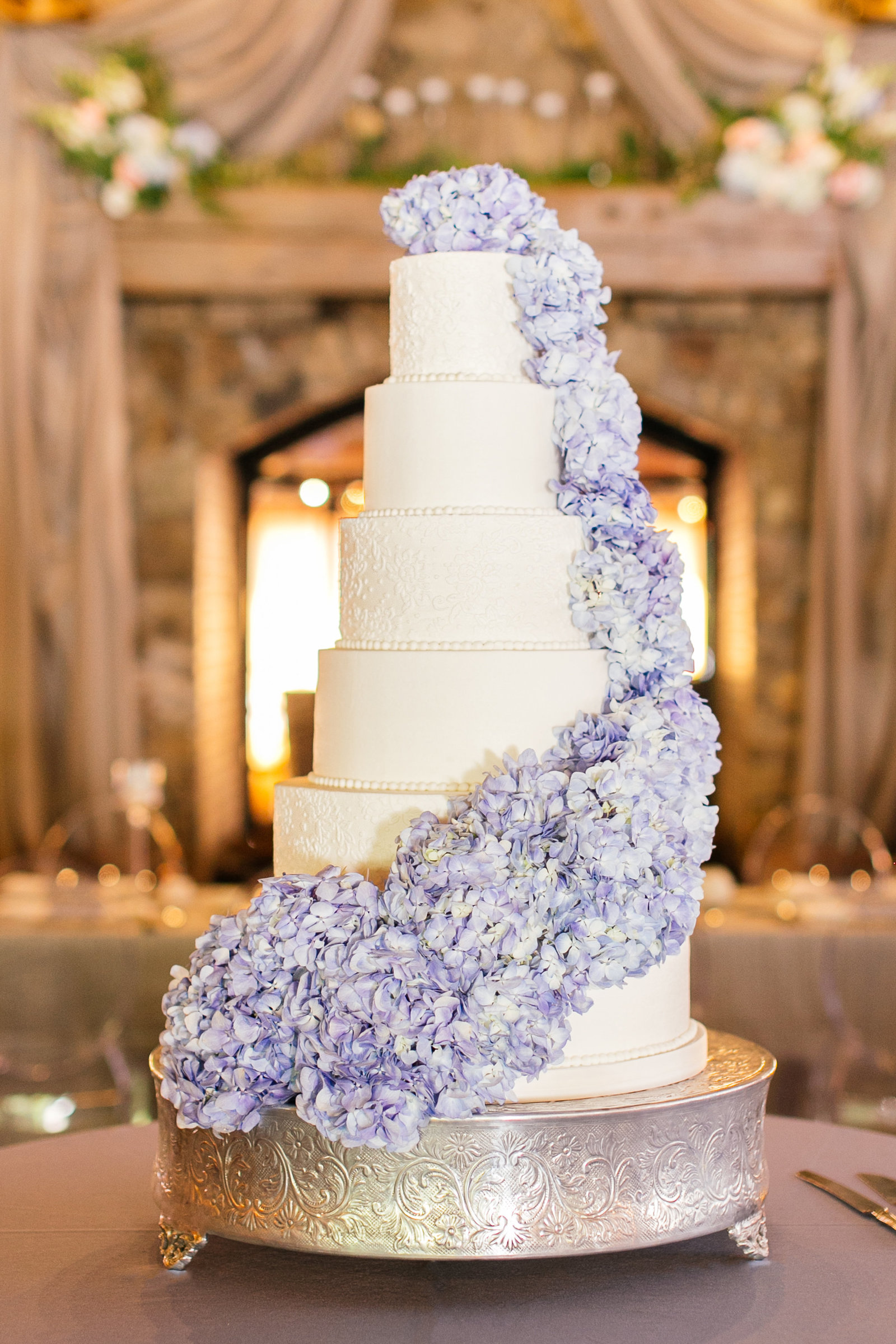 Elegant grand white buttercream wedding cake with lace details and blue hydrangea cascade at Angus Barn Pavilion McLean Events