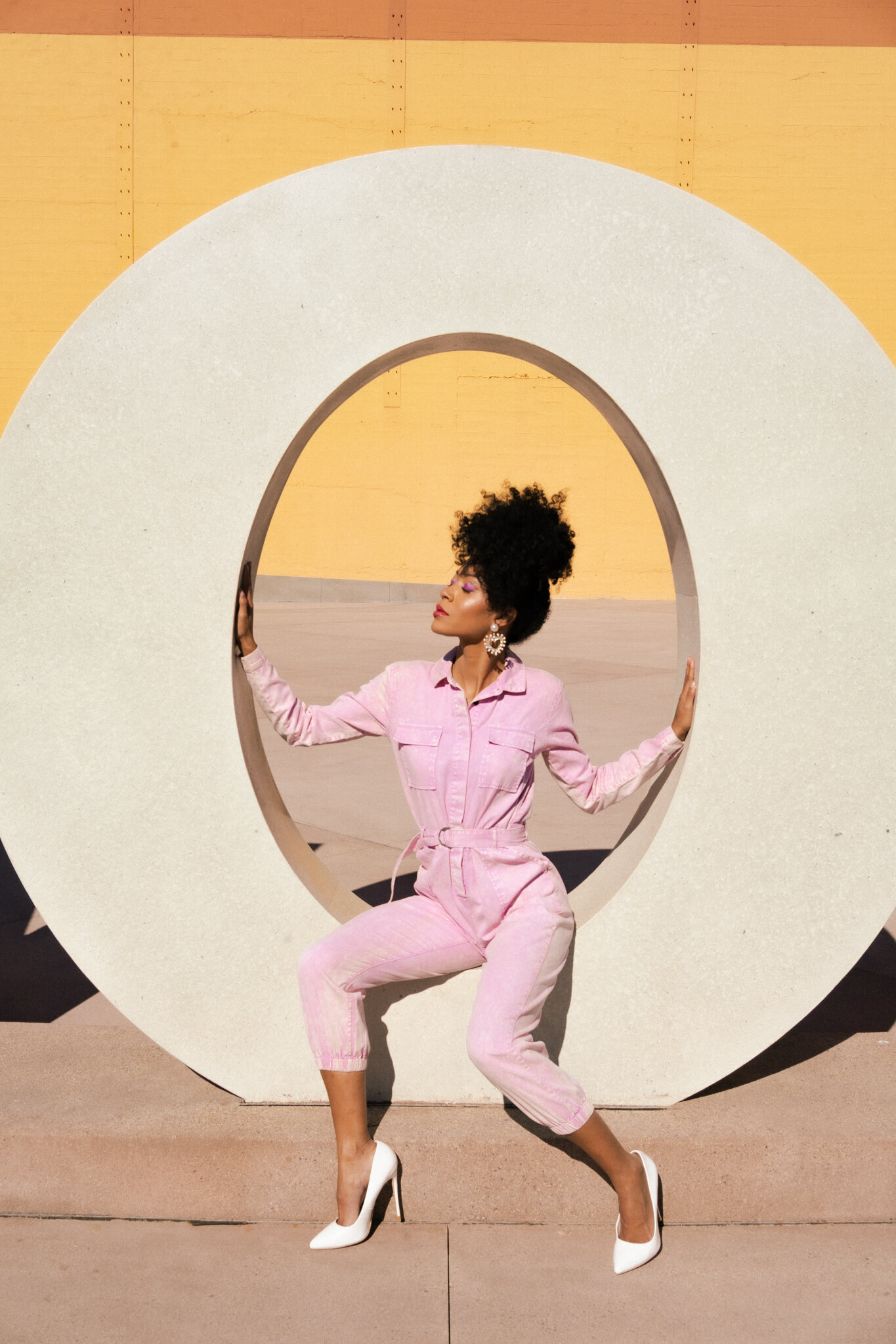 female model in pink denim jumpsuit sitting in the middle of an o shaped statue