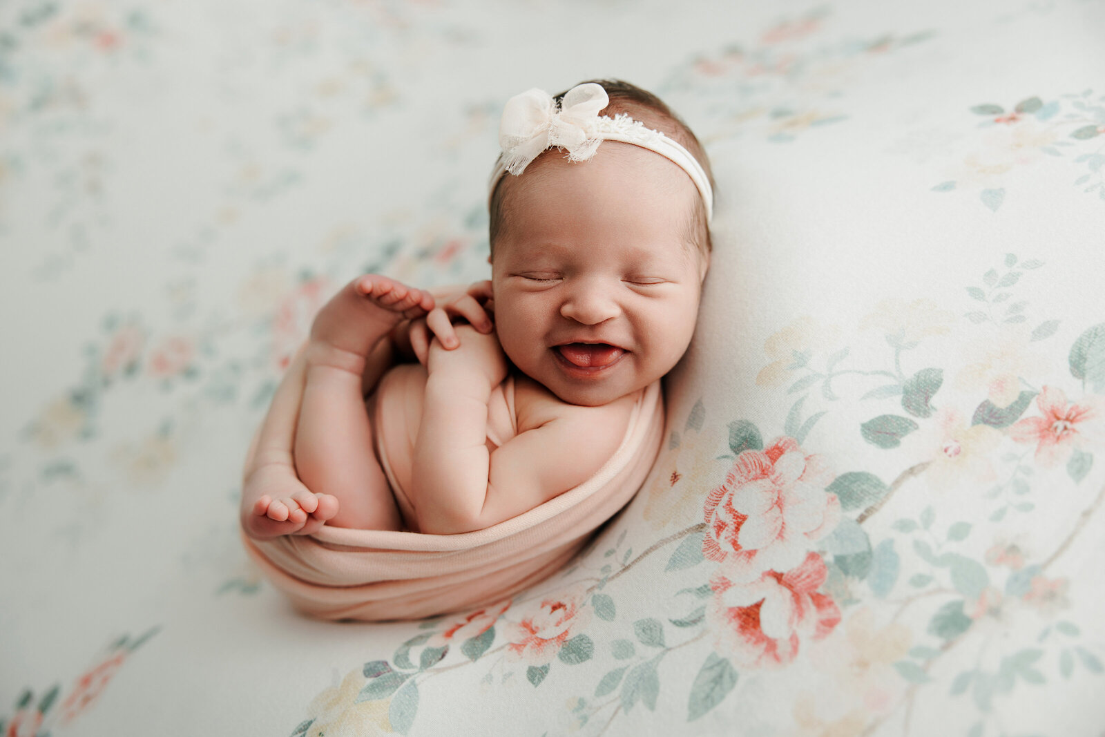 A baby girl smiles broadly on a floral backdrop