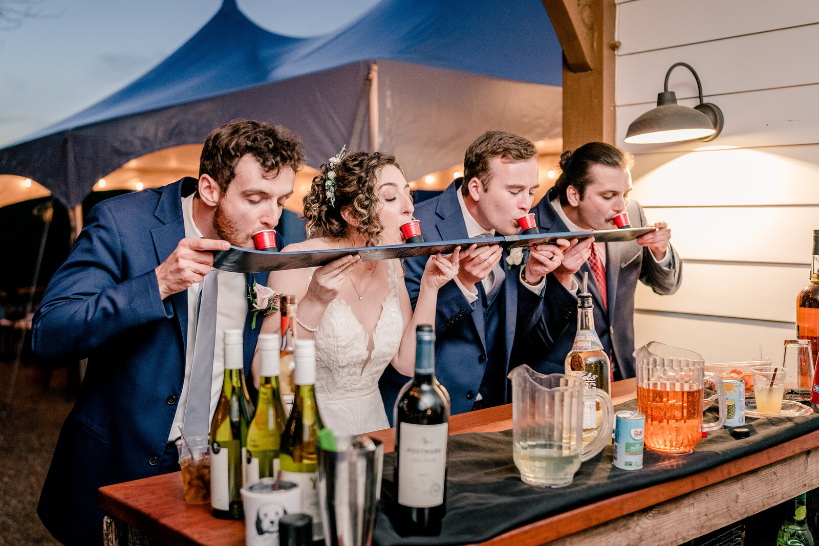 A bride and groom with their friends doing a shot ski during their wedding at Blue Hill Farm in Northern Virginia