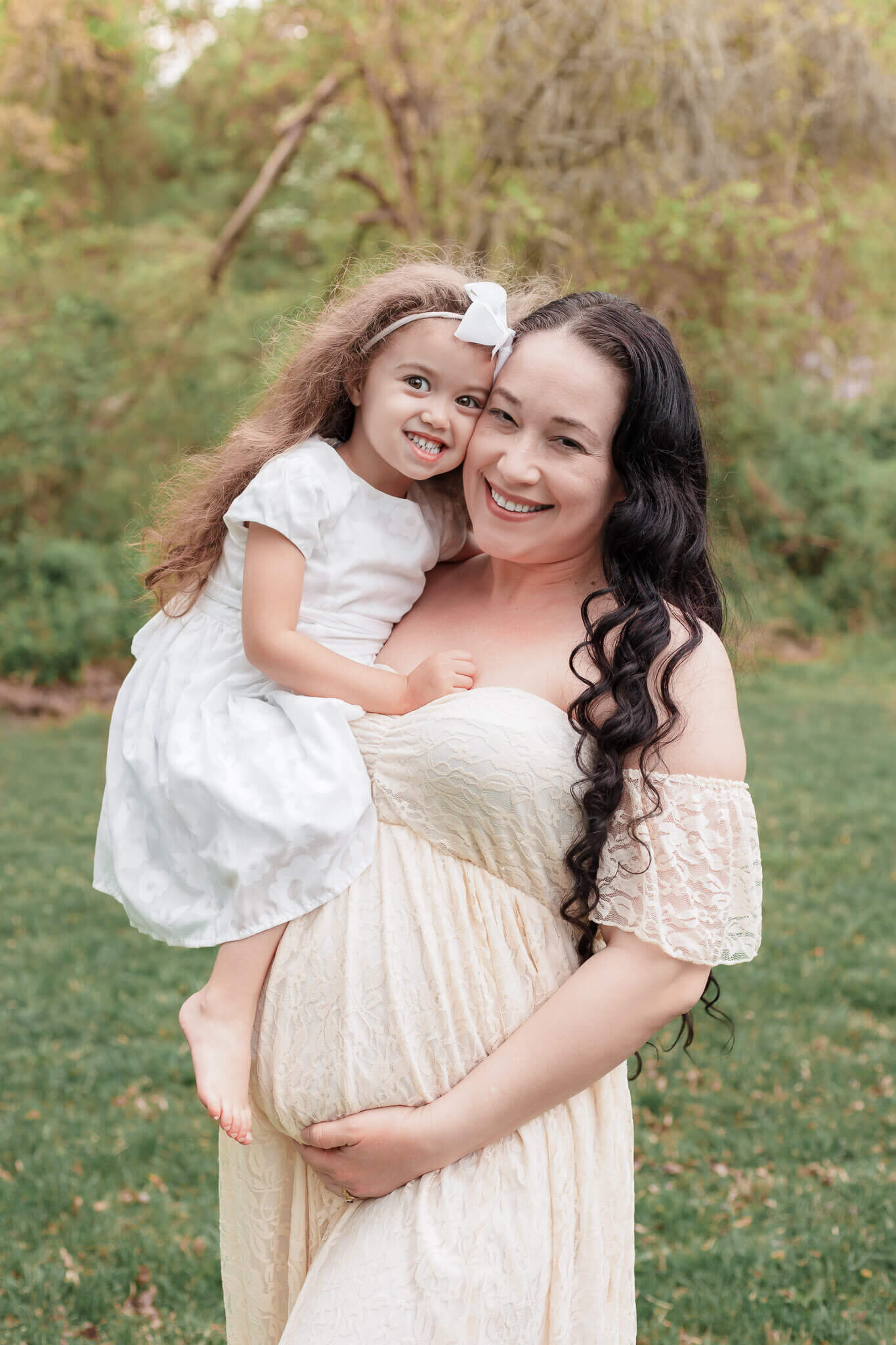 A mother-to-be and her older daughter snuggling and smiling at the camera.