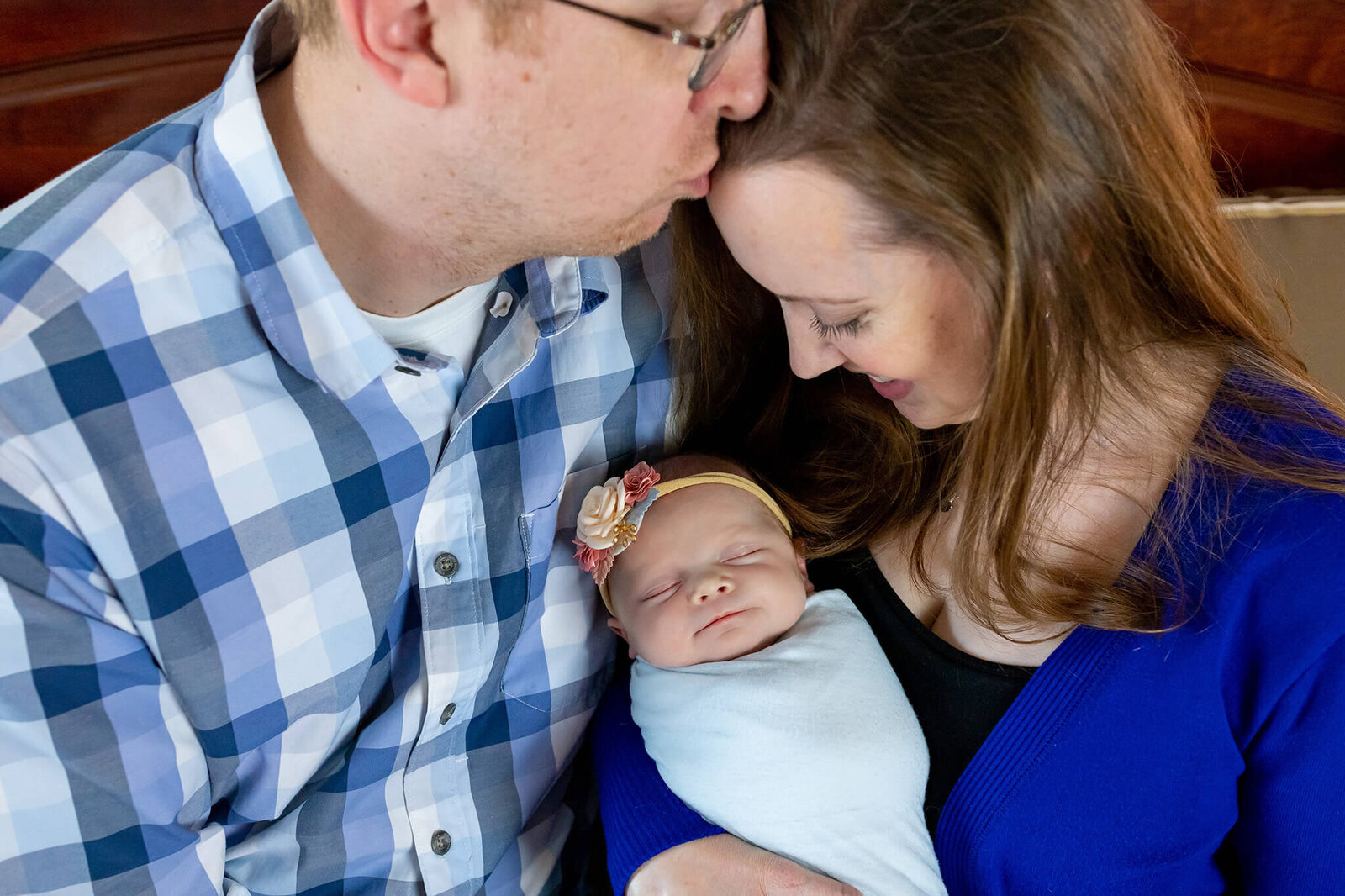 A Manassas couple snuggling their newborn and dad kissing mom's forehead.