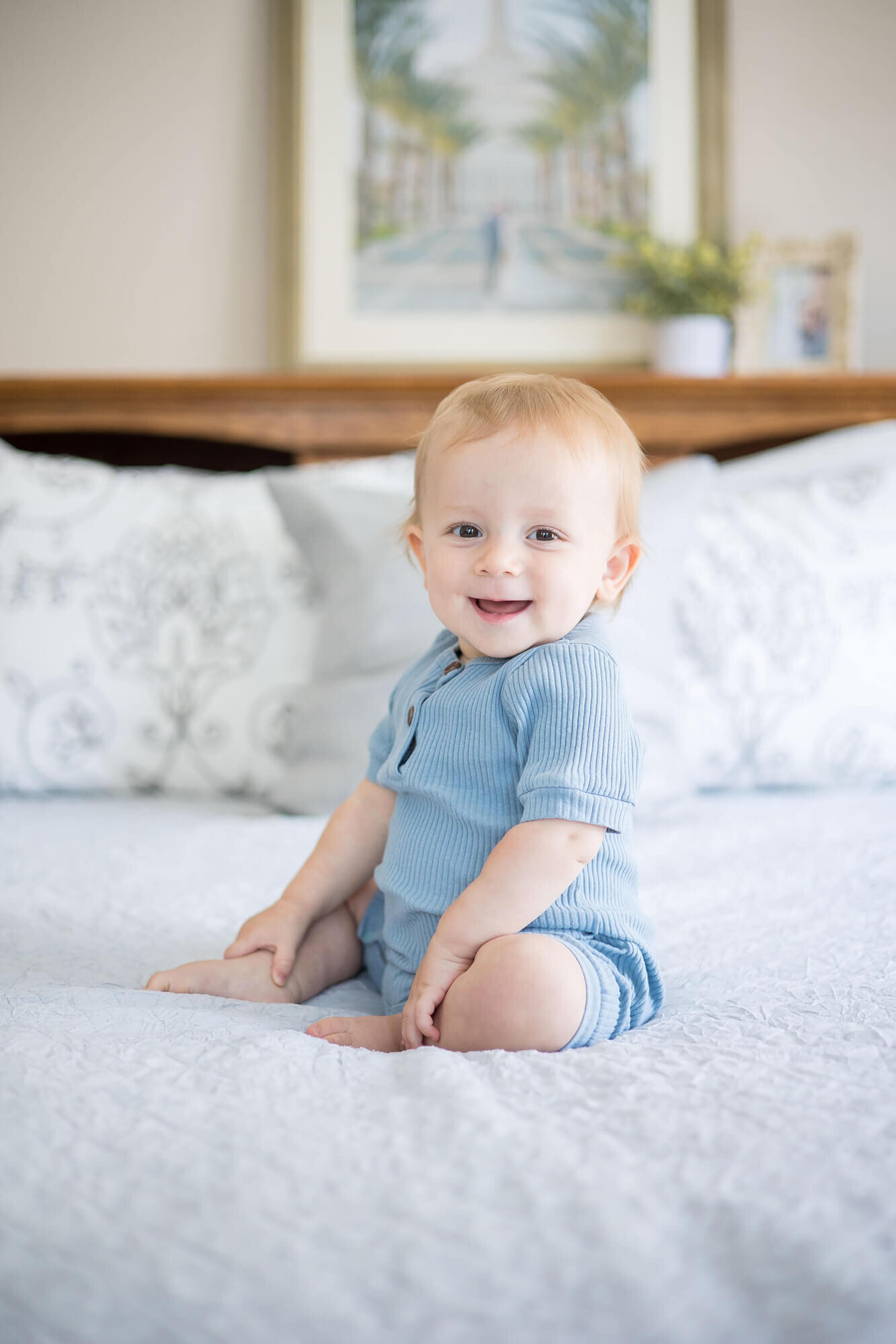 excited and happy baby boy in blue sitting on a bed,  captured by las vegas milestone photographer Jessica Bowles