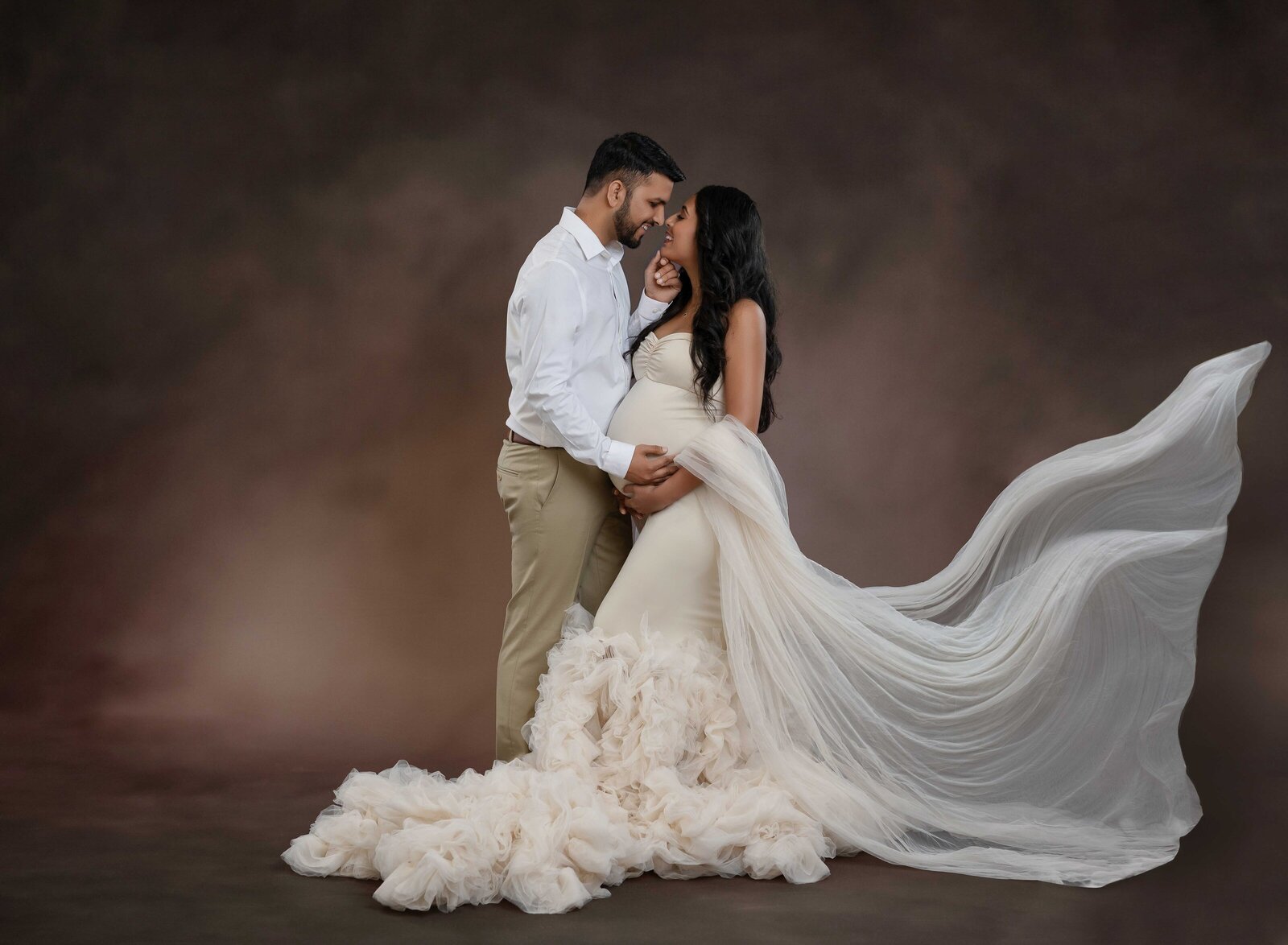 Man and women at maternity photo studio, taking portrait as Dad holds Mom's chin and touches noses.