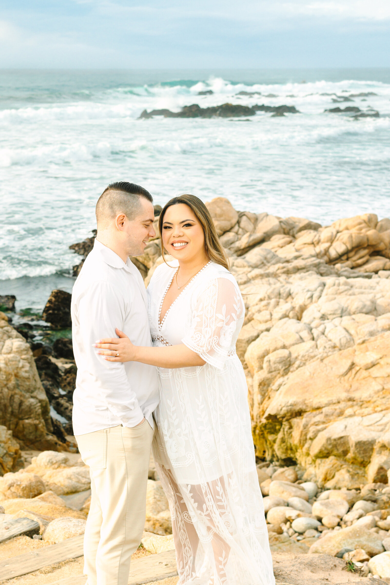 An engaged man and woman take photos on the beach in Pacific Grove, Monterey, California near Big Sur.