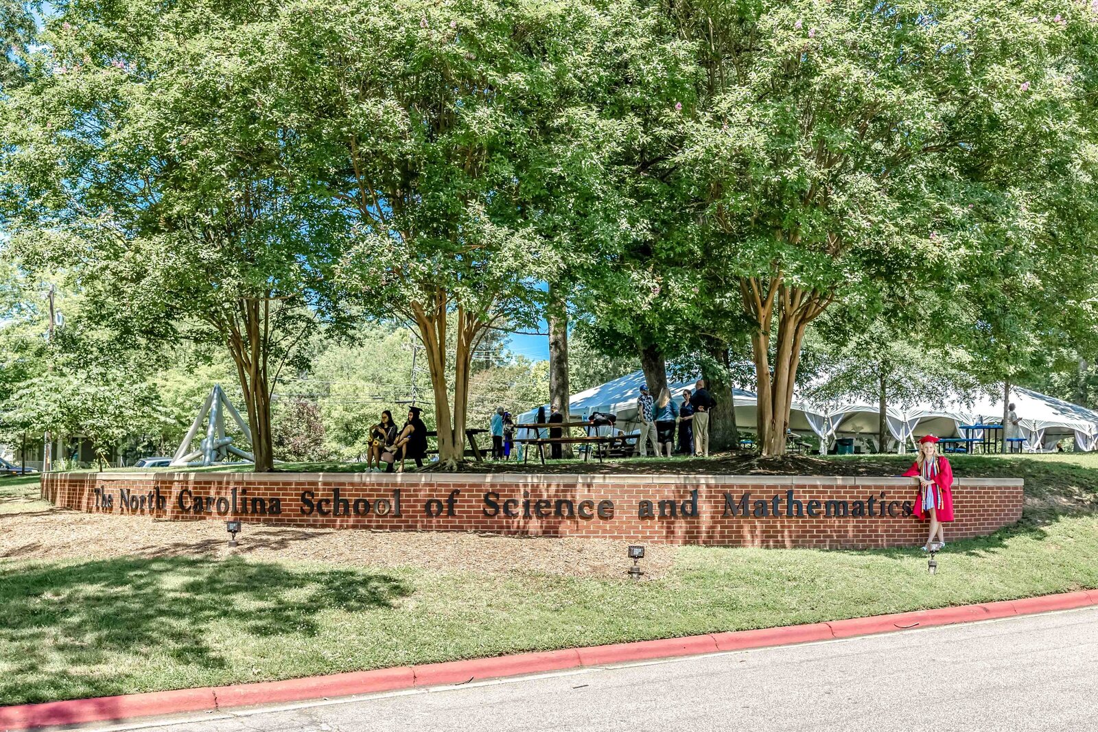 The entrance sign for the North Carolina School of Science and Mathematics surrounded by trees with people gathering nearby in North Carolina. This image captures the academic environment, ideal for school event photography.