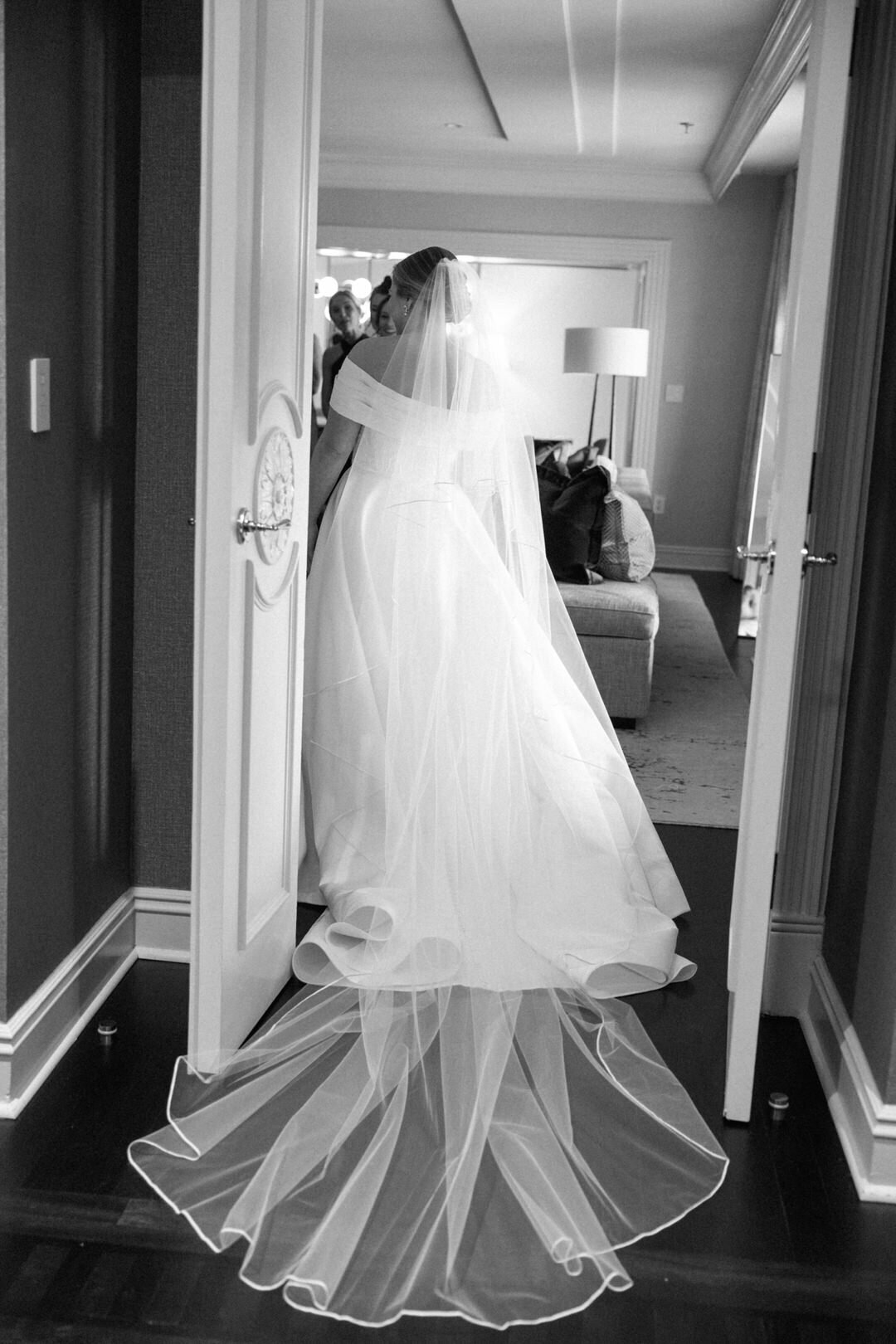 Black and White of Bride Walking Through doorway with Veil Trailing