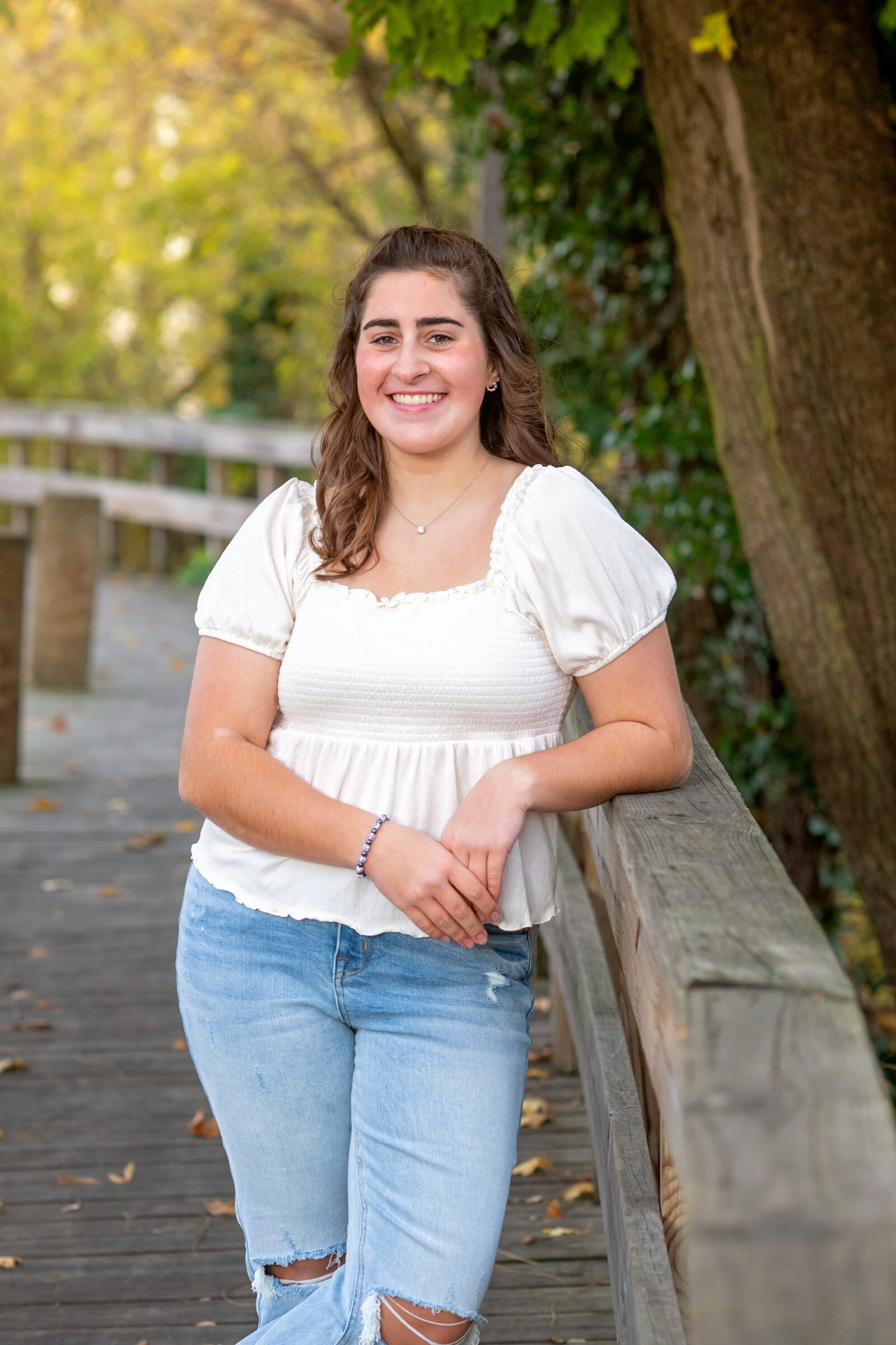 smiling high school senior leans on wooden walk way in cuyahoga falls