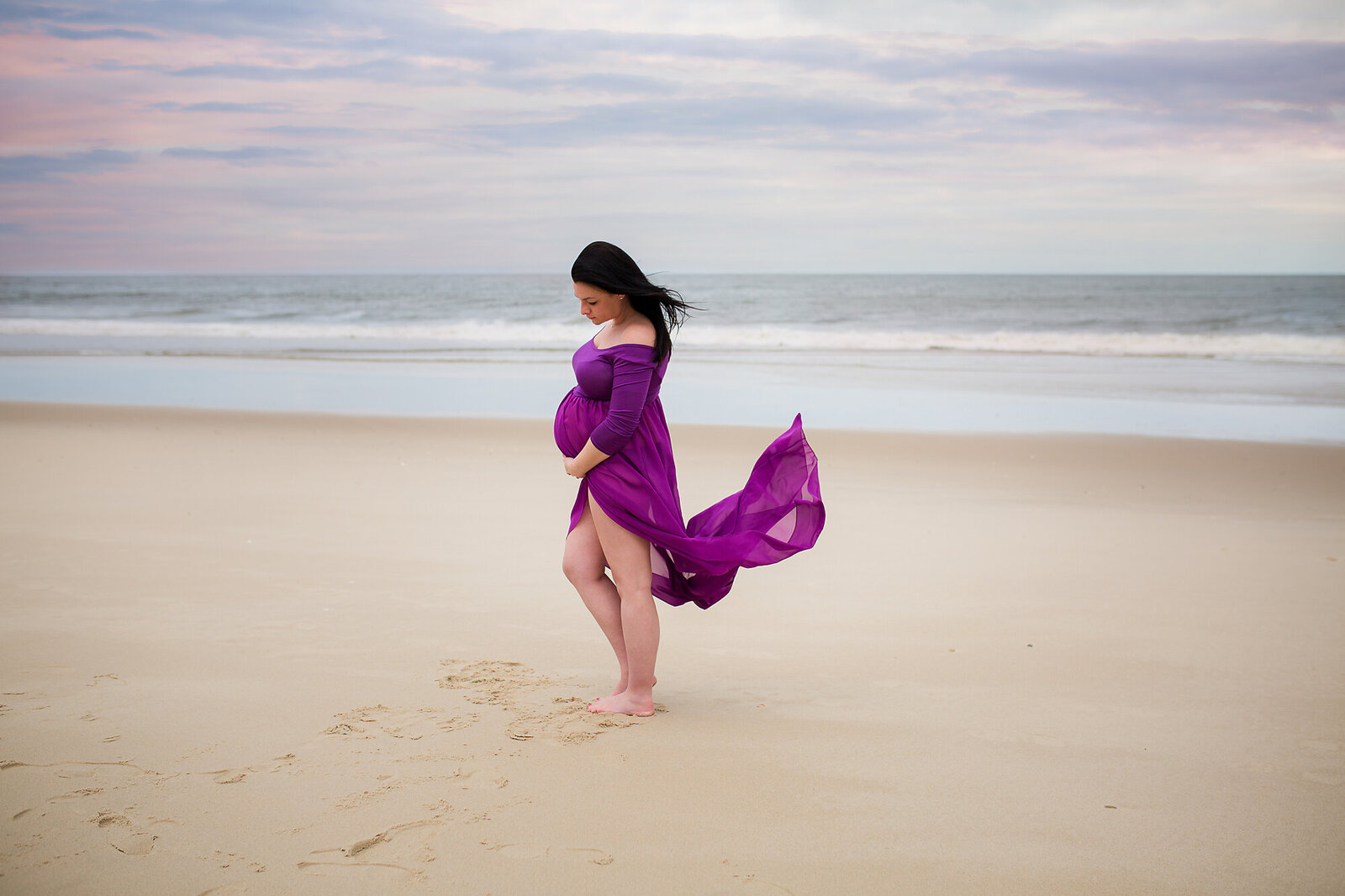 mom in purple dress blowing in the wind on the beach