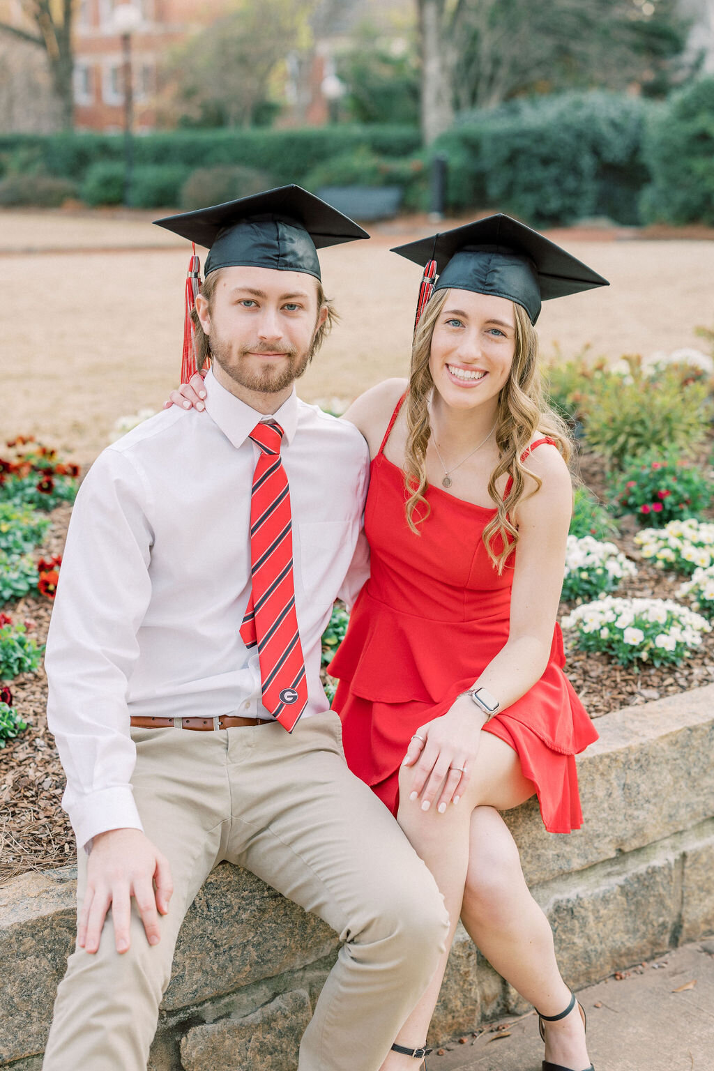 Girl and guy wearing graduation outfits and caps sit on campus of University of Georgia