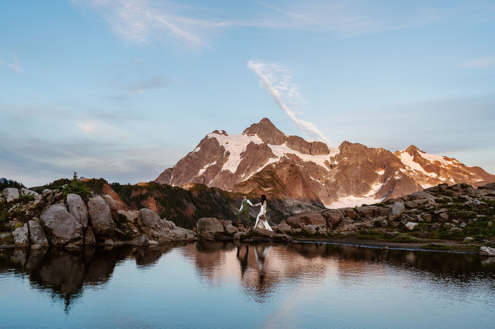 a couple walks along a ridgeline and is reflected in a lake in the North Cascades during their Washington elopement