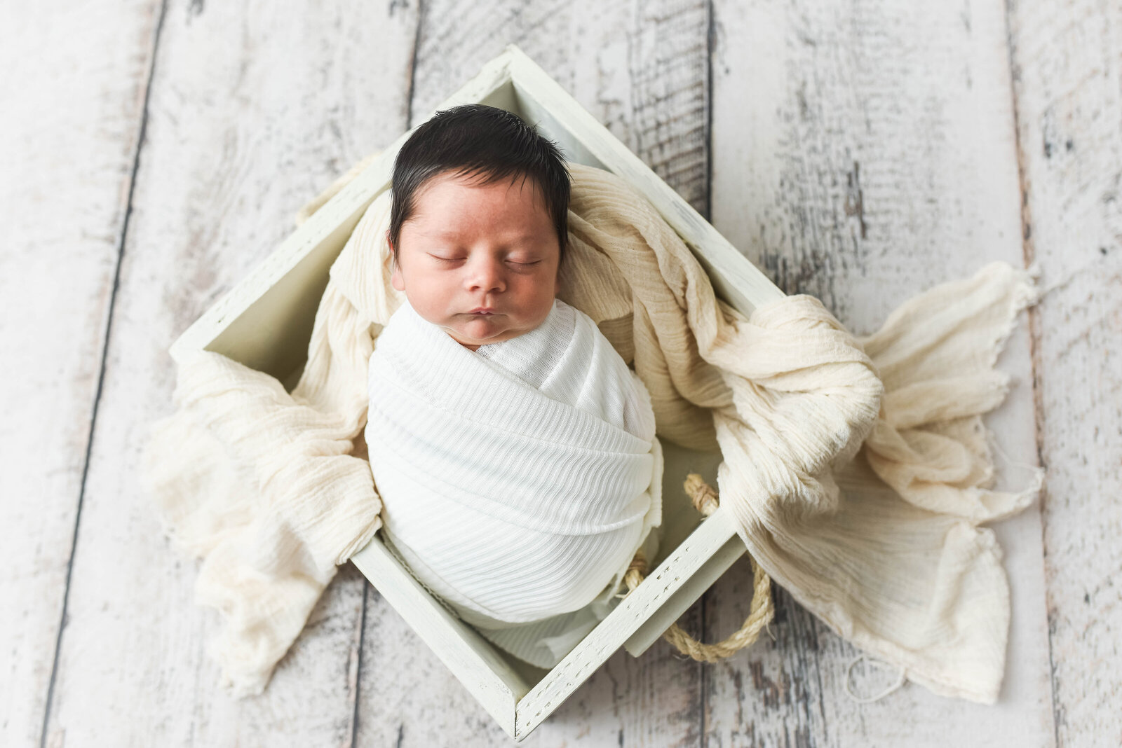 newborn baby laying in a basket swaddled in a white blanket