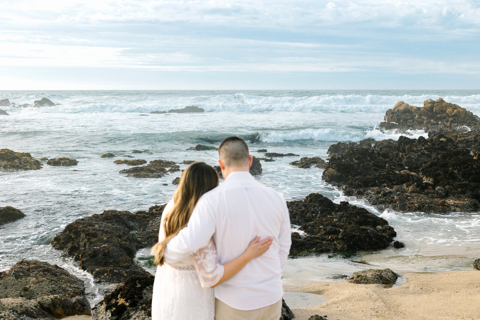 An engaged man and woman take photos on the beach in Pacific Grove, Monterey, California near Big Sur.