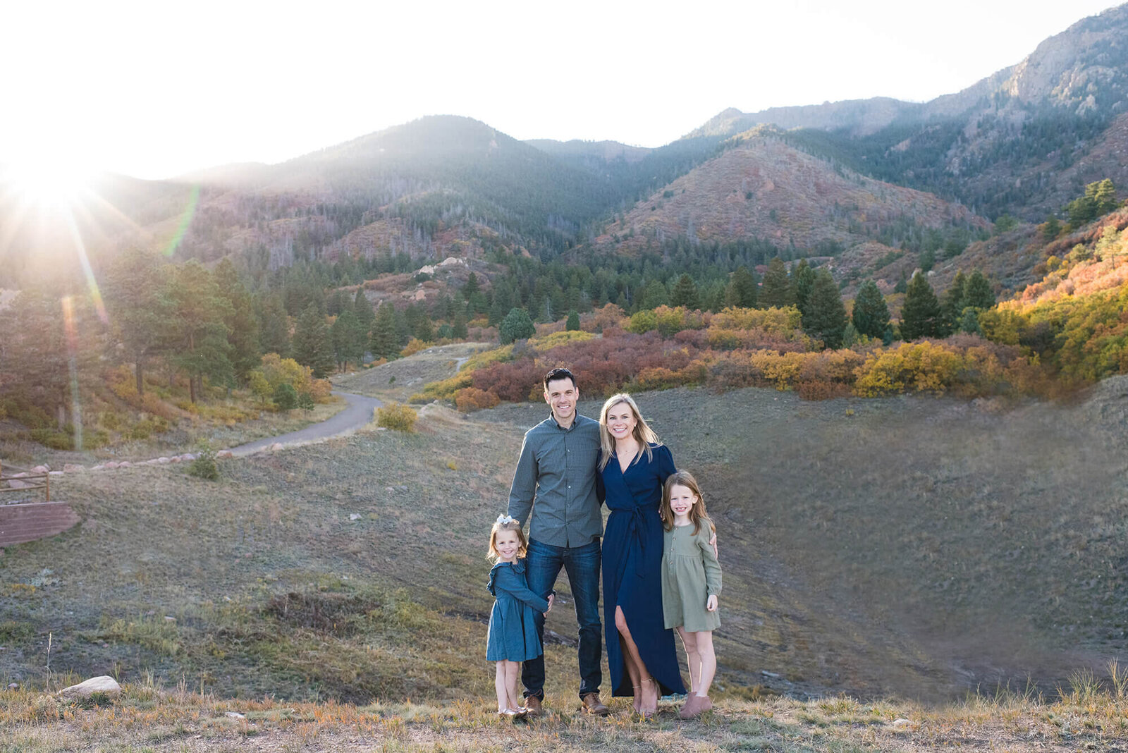 A family of 4 stand in a gravel trail hugging at sunset