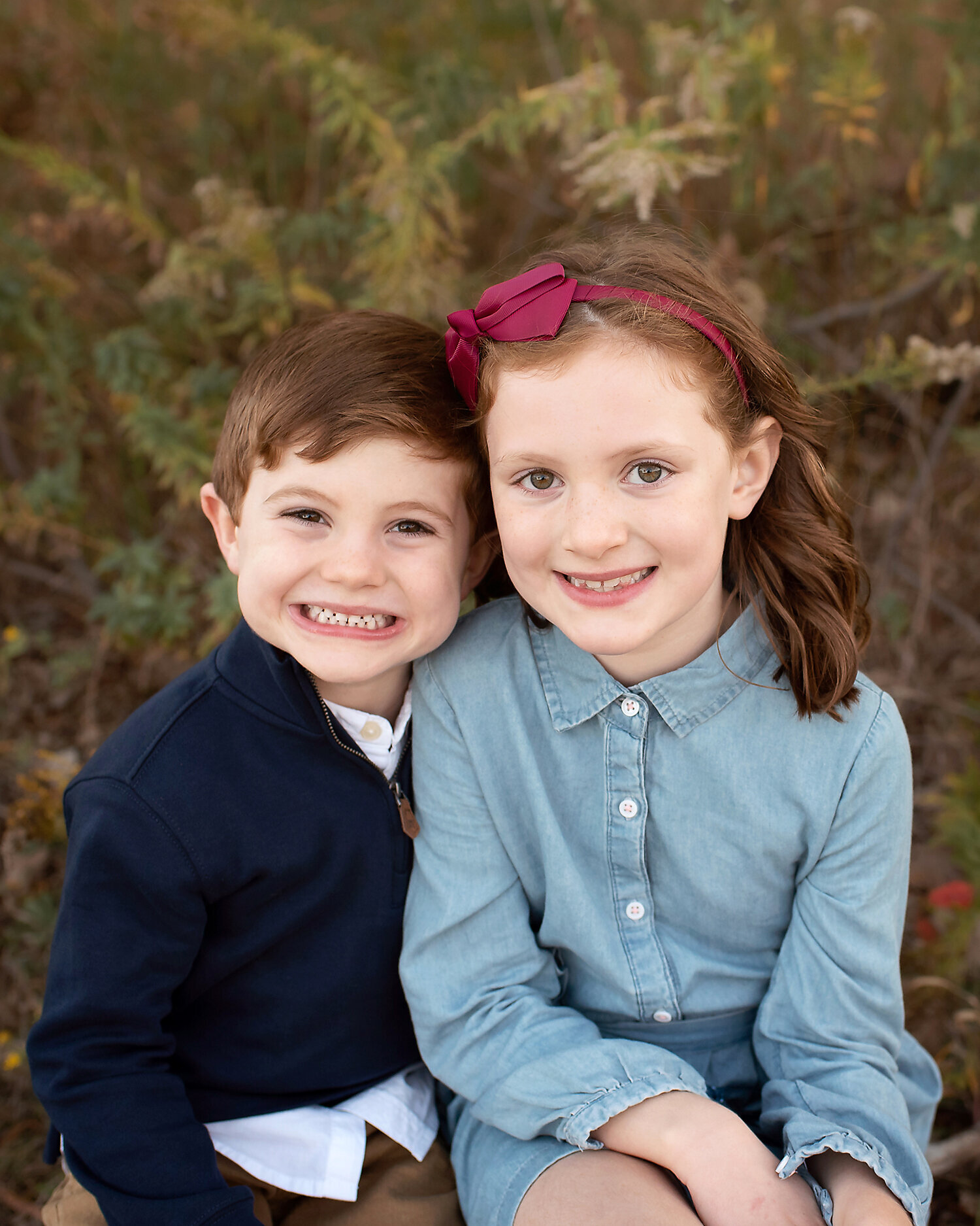 Brother and sister sitting close and smiling at their outdoor photo shoot.