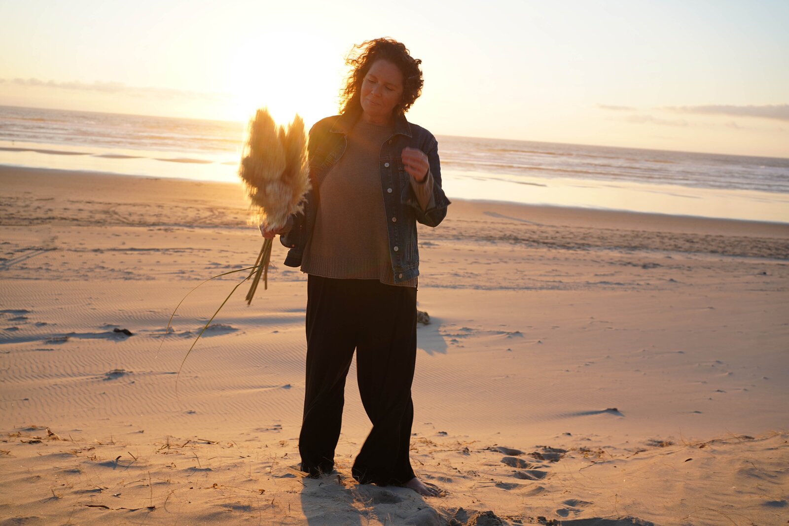 Woman gazing at pampas grass bundle in front of a beach sunset